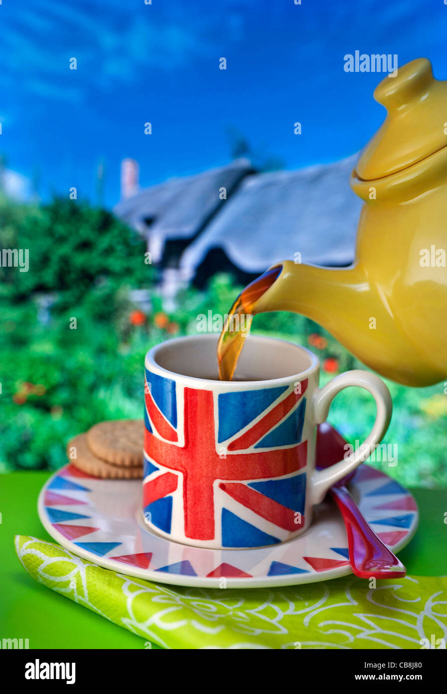 ENGLISCHES TEE-GIESSHAUS-STAYCATION-KONZEPT. Englische Union Jack Themen Tasse Tee und Kekse, typische Reetgedeckten Hütte und Garten Hintergrund Großbritannien Stockfoto