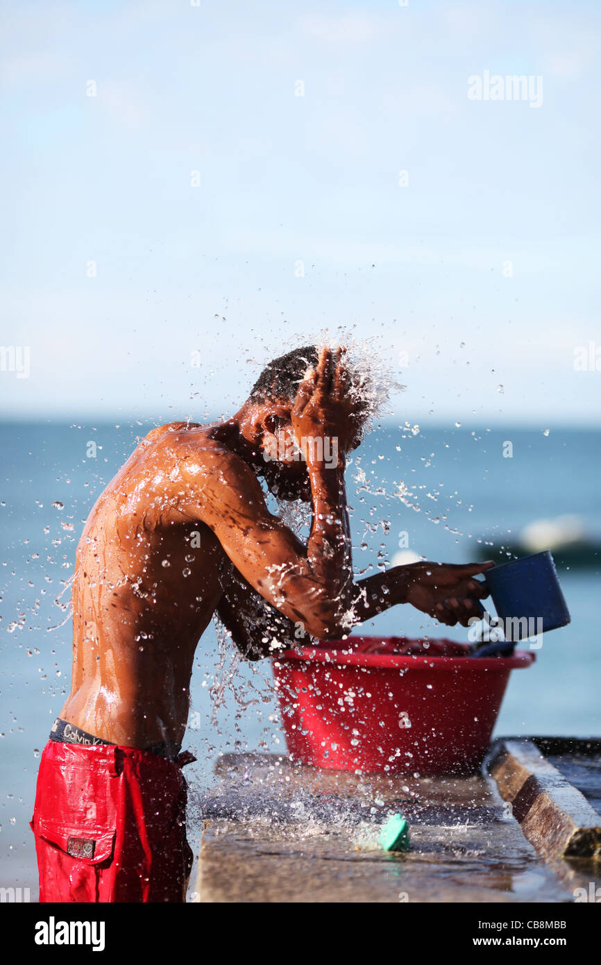 Madagassischer junger Mann wäscht sich spülen frisches Wasser aus einem Plastikeimer in Nosy Komba, Nordküste westlichen Madagaskar, Afrika Stockfoto