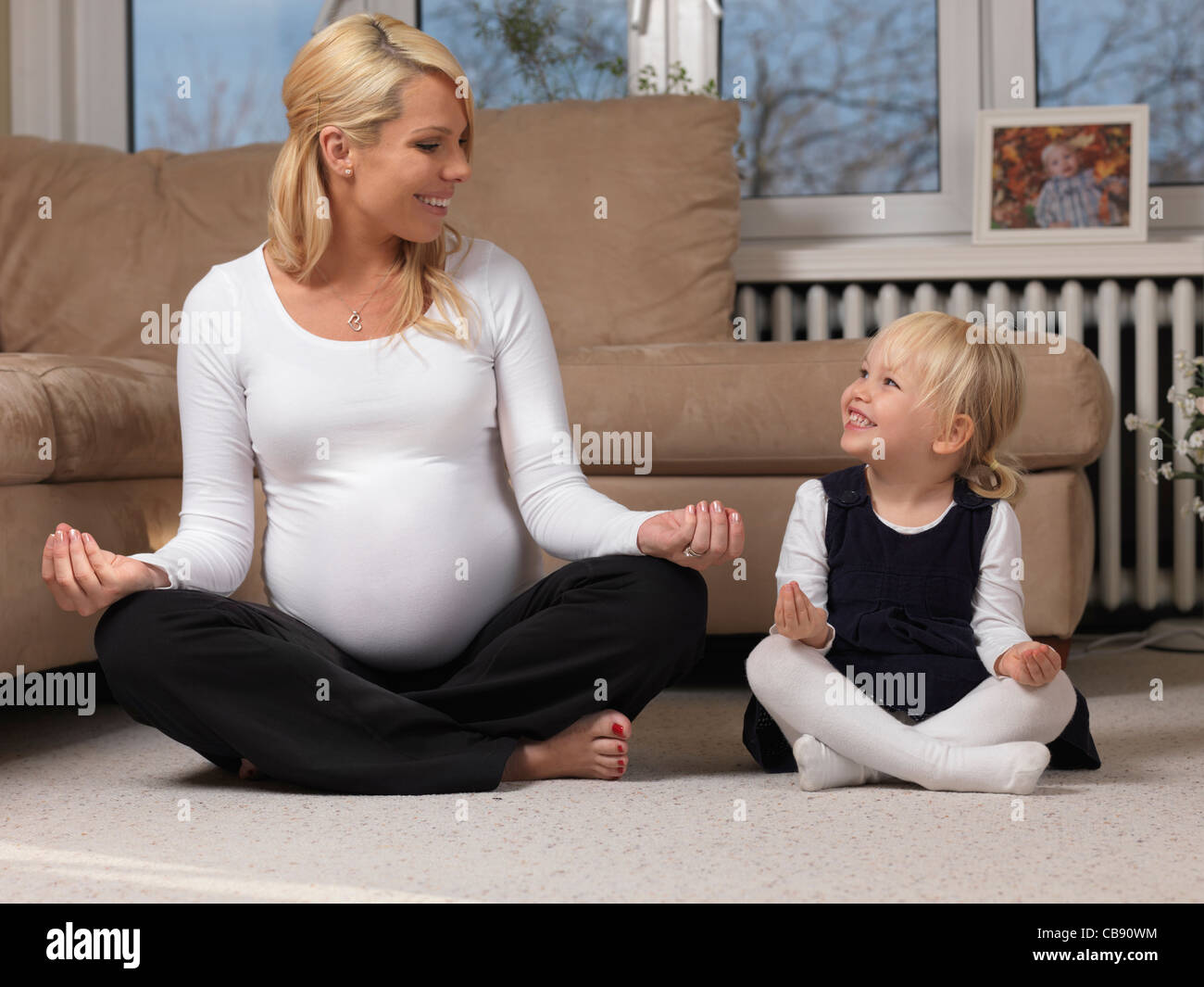 Glückliche schwangere Mutter und ihre kleine Tochter gemeinsam Spaß haben beim Yoga zu Hause Stockfoto
