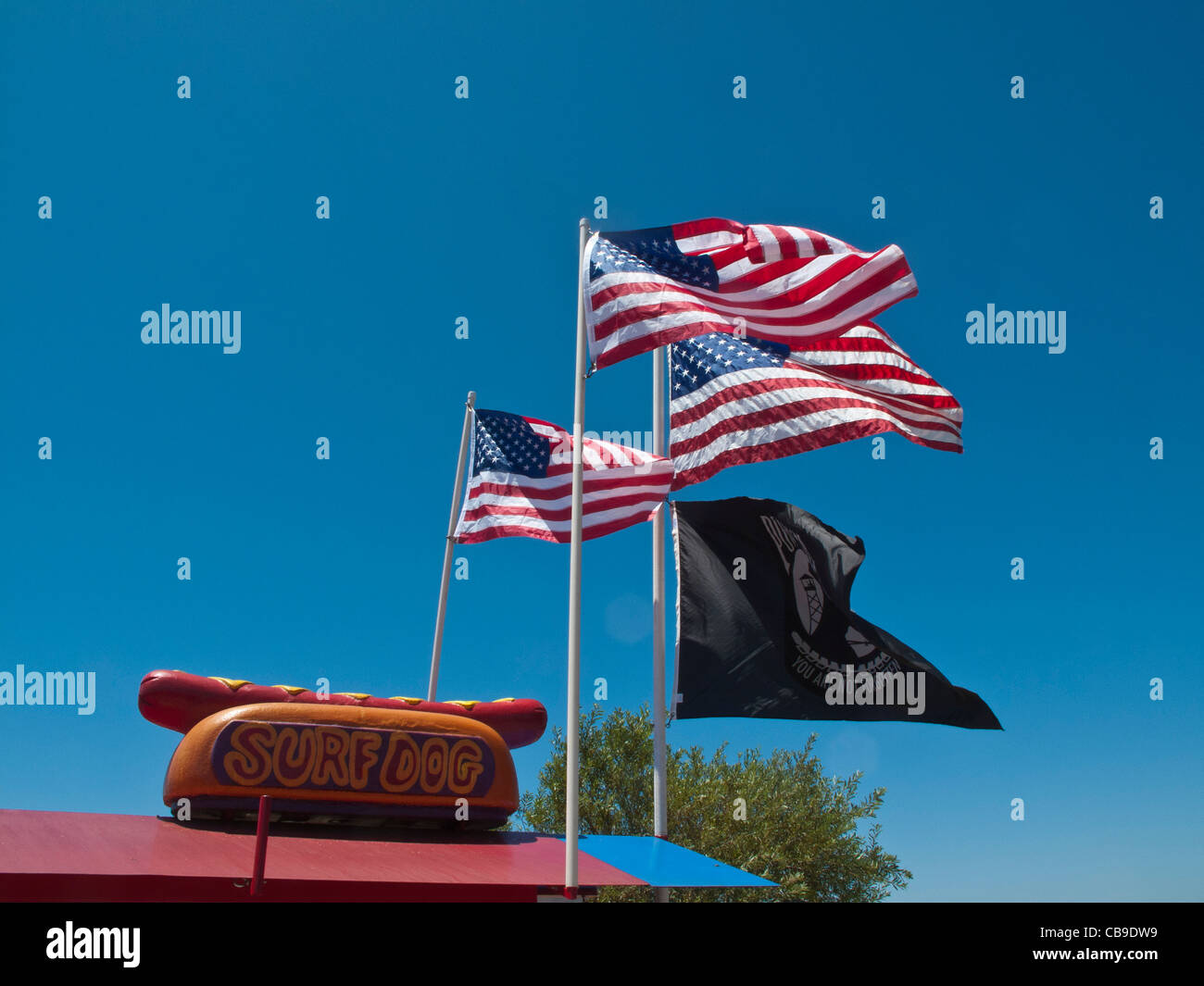 Vier Flaggen wehen über dem Surf Dog Hotdog Stand Schild, einen Hot Dog in einem Brötchen, direkt an der Autobahn 101 in Carpinteria, Kalifornien. Stockfoto