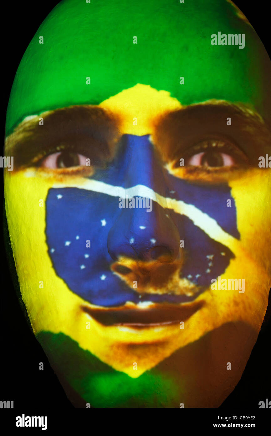 Riesige Skulptur eines Gesichts beleuchtet durch ein Bild von einem brasilianischen Fahne bemaltem Gesicht während des Festival of lights 2011 in Berlin Stockfoto