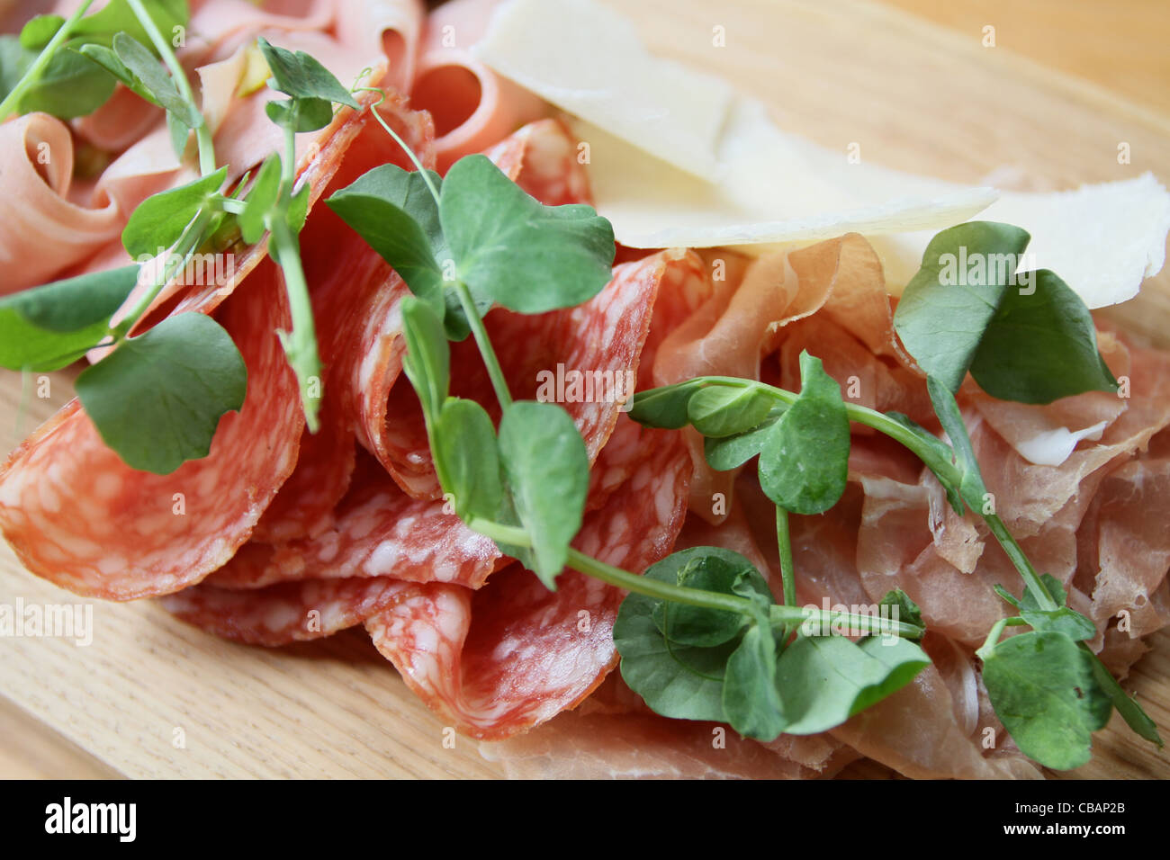 Salami-Parma-Schinken-Platte mit Erbsensprossen auf einem hölzernen Teller serviert Stockfoto