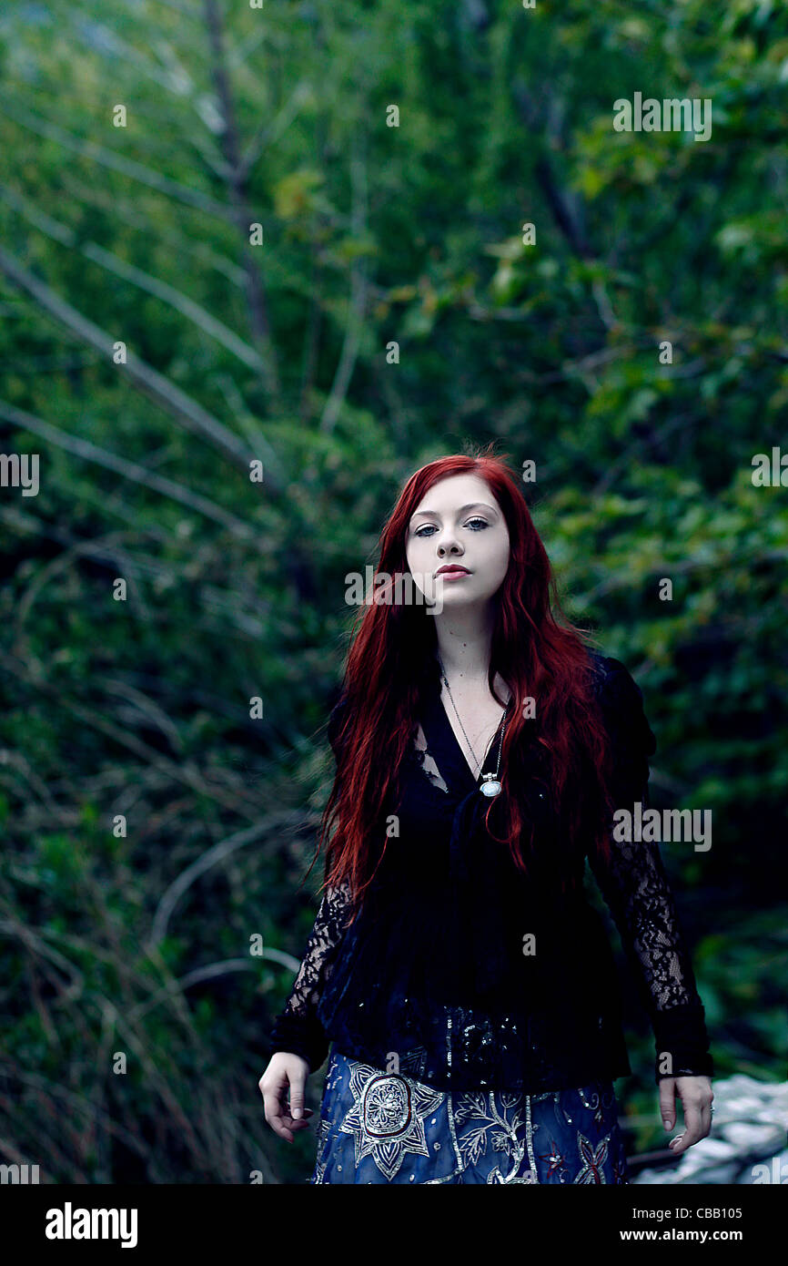 Ein Mädchen mit roten Haaren allein im Wald mit Bäumen hinter ihr Stockfoto