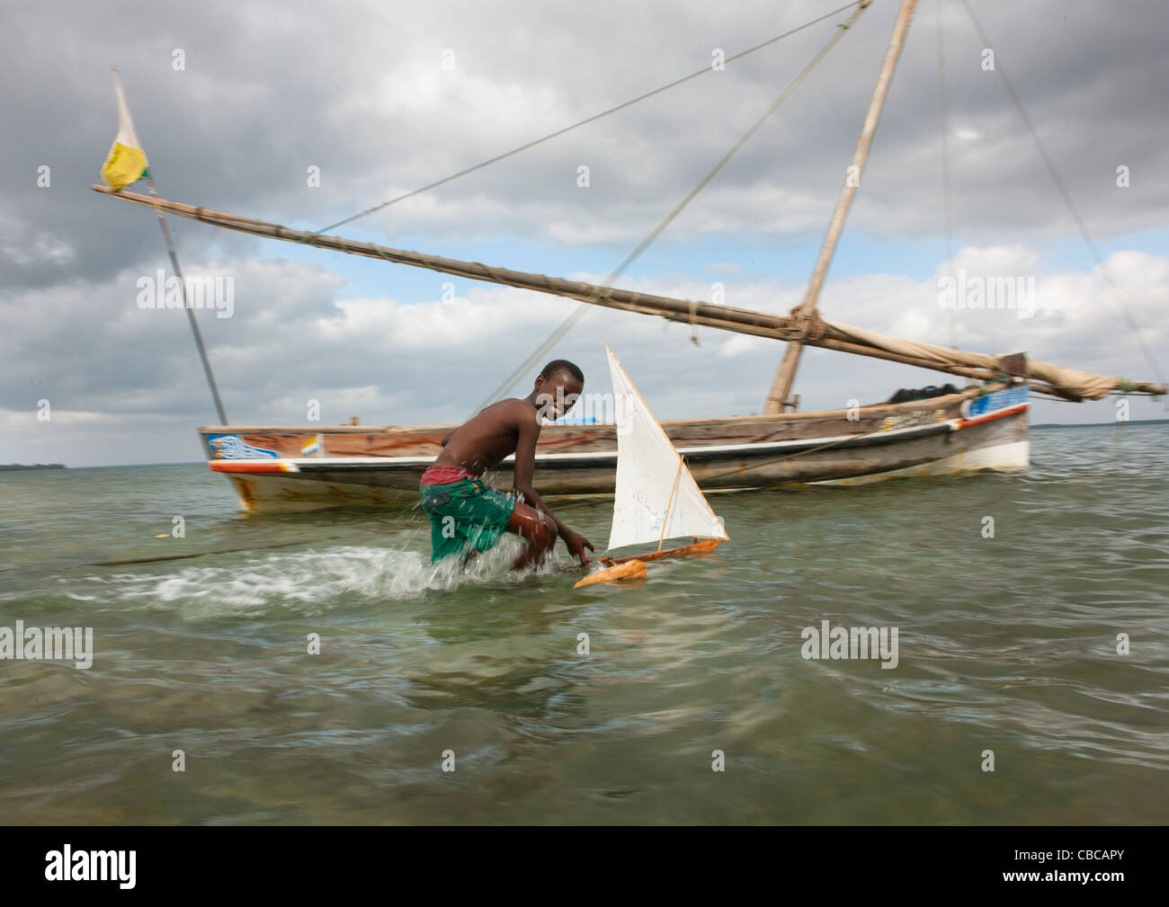 Kleiner Junge spielt mit Dhow Modell entlang der Meeresküste, echten Dhau im Hintergrund, Lamu, Kenia Stockfoto
