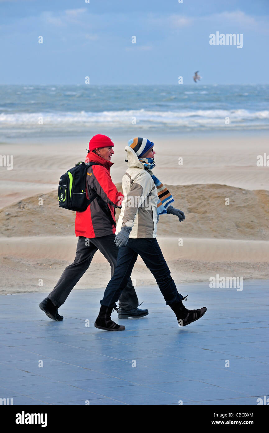 Paare, die im Winter am Deich bei stürmischem Wetter entlang der Nordsee an Nieuwpoort, Belgien Stockfoto