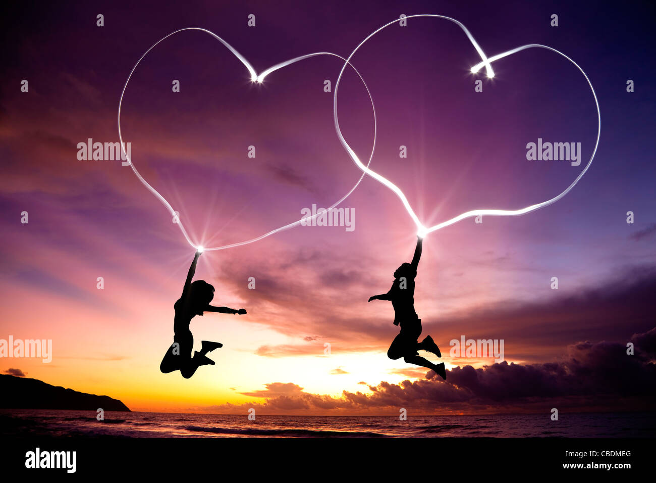 junges Paar springen und Zeichnung verbundene Herzen von Taschenlampe in der Luft am Strand vor Sonnenaufgang Stockfoto