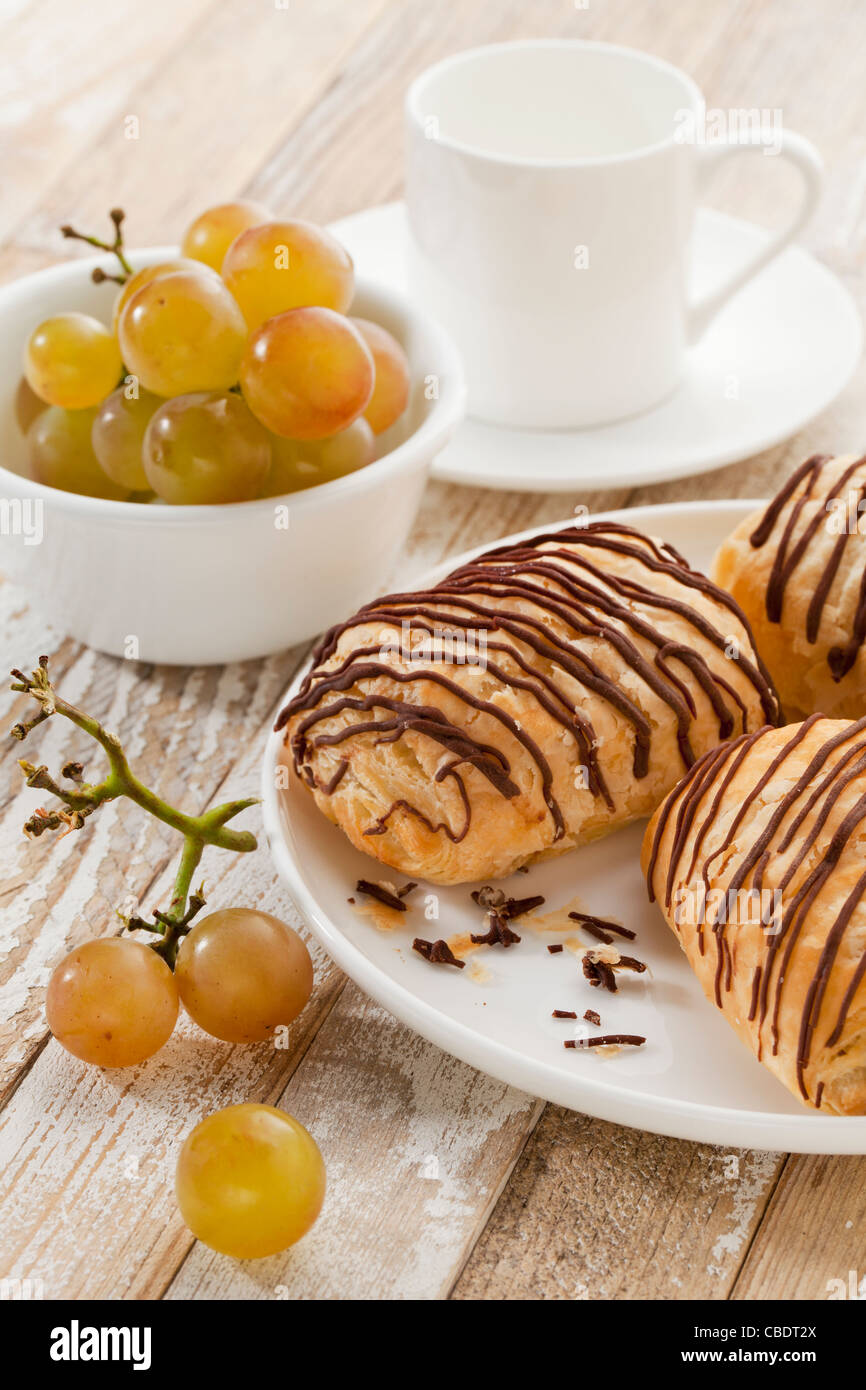 Mini-Schoko-Croissants, Trauben und Kaffeetasse auf einem rustikalen Holztisch Stockfoto