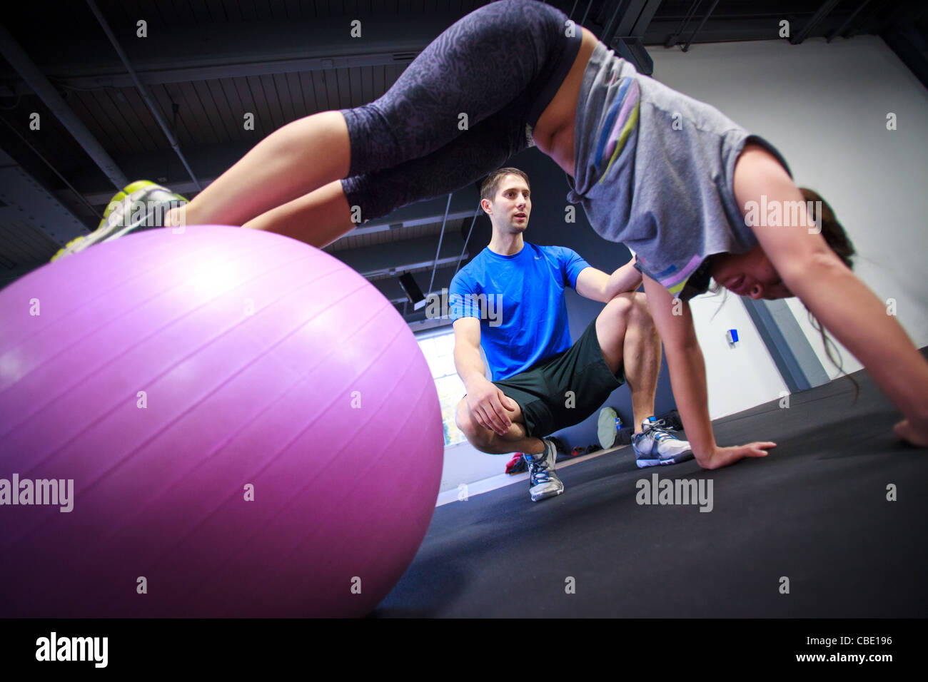 Junge Asiatin wird von personal Trainer dabei Liegestütze auf einer Yoga-Ball trainiert. Stockfoto