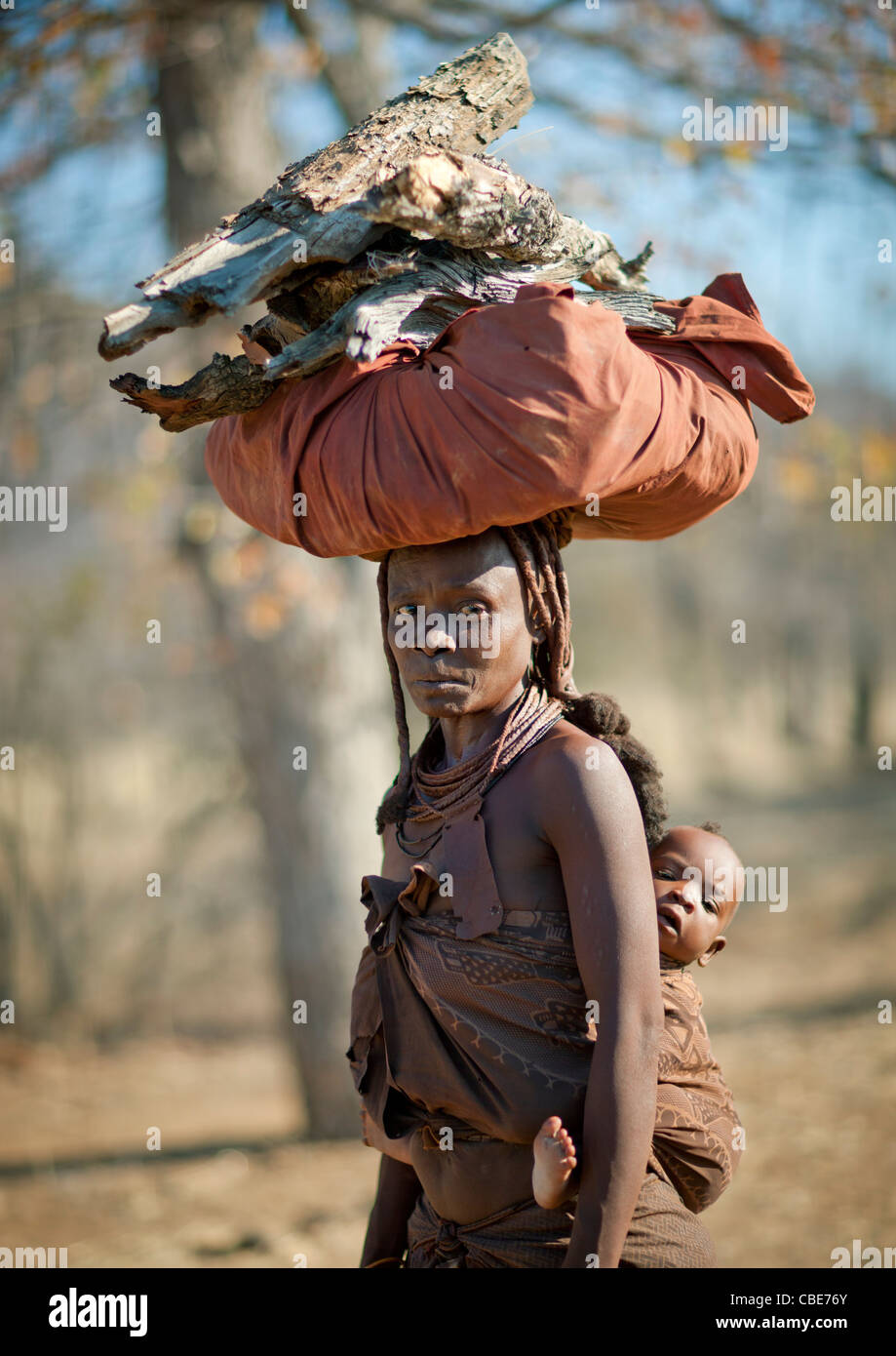 Muhimba Frau mit ihrem Baby auf dem Rücken tragen Holz auf dem Kopf, Dorf Elola, Angola Stockfoto