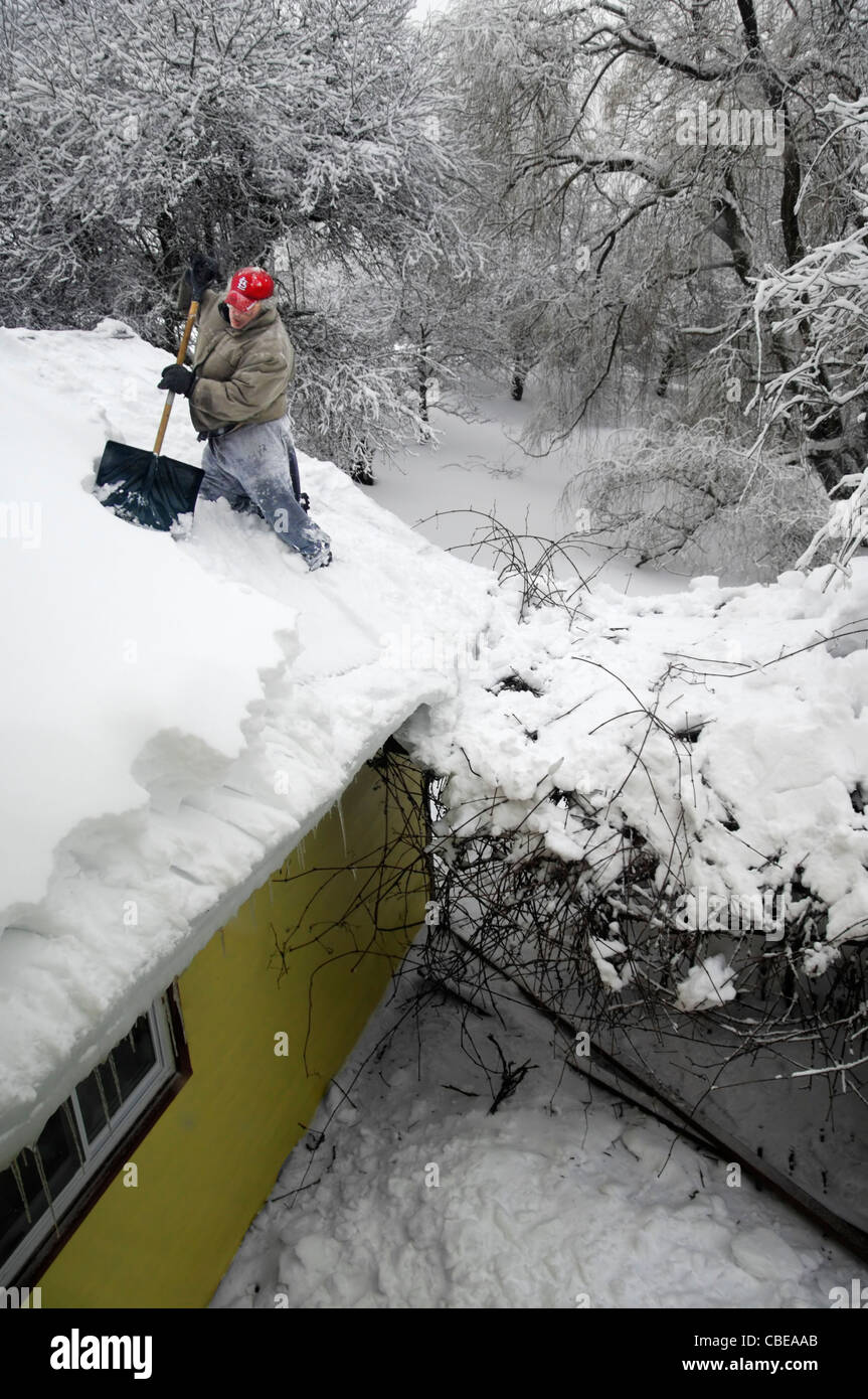 Ein Mann Schaufeln Schnee vom Dach eines Hauses Stockfoto