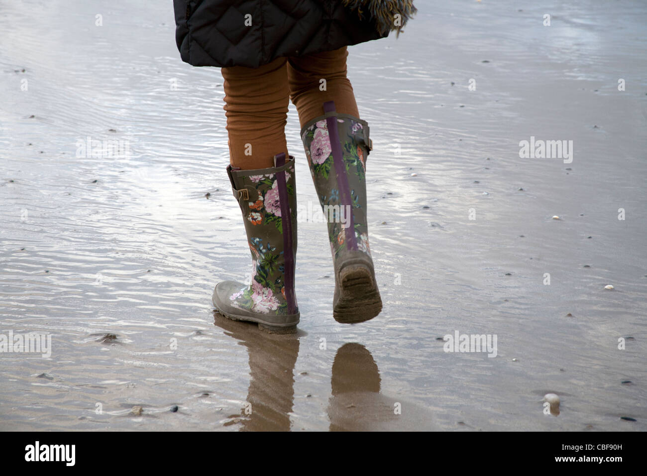 Eine Frau trägt Gummistiefel in Fleetwood während des Gehens eines Hundes, Lanccashire, UK Stockfoto