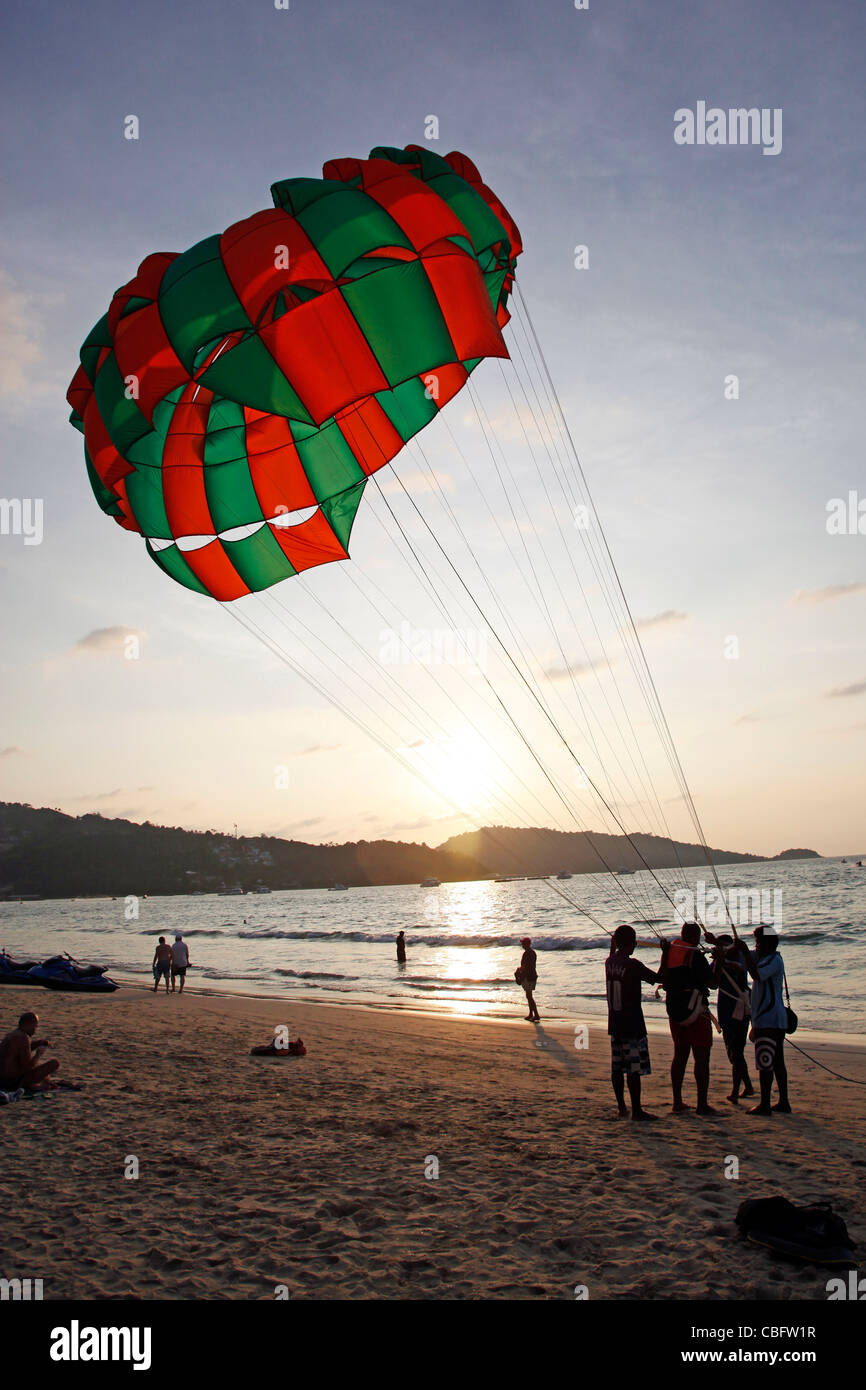 Menschen in der Silhouette bei Sonnenuntergang parasailing mit einem Fallschirm, eines der touristischen Sportaktivitäten am Patong Beach, Patong, Phuket Stockfoto