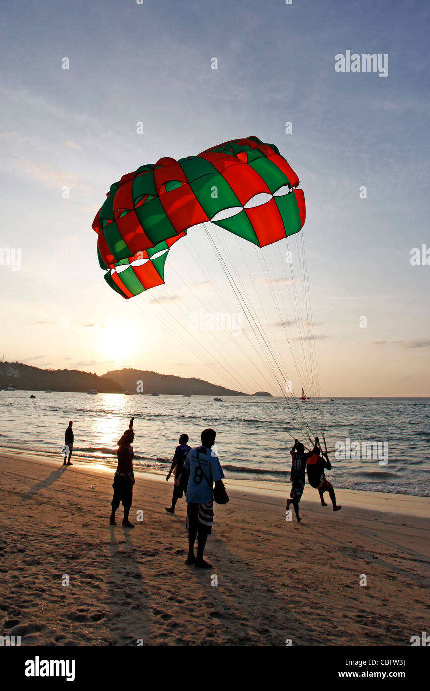 Menschen in der Silhouette bei Sonnenuntergang parasailing mit einem Fallschirm, eines der touristischen Sportaktivitäten am Patong Beach, Patong, Phuket Stockfoto
