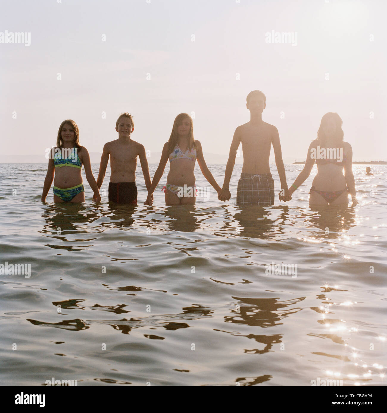 Fünf Freunde Hand in Hand in Folge beim Waten im Meer Stockfoto