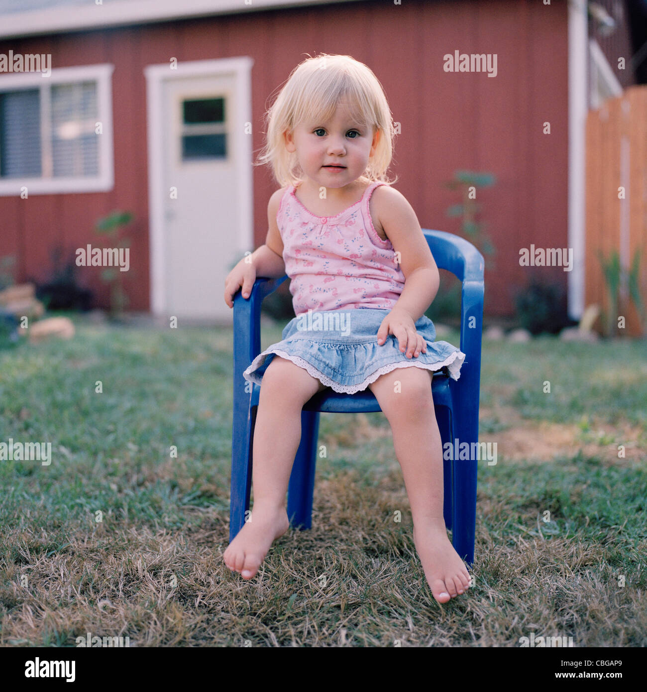 Ein kleines Mädchen sitzt auf einem Plastikstuhl in einem Hof Stockfoto