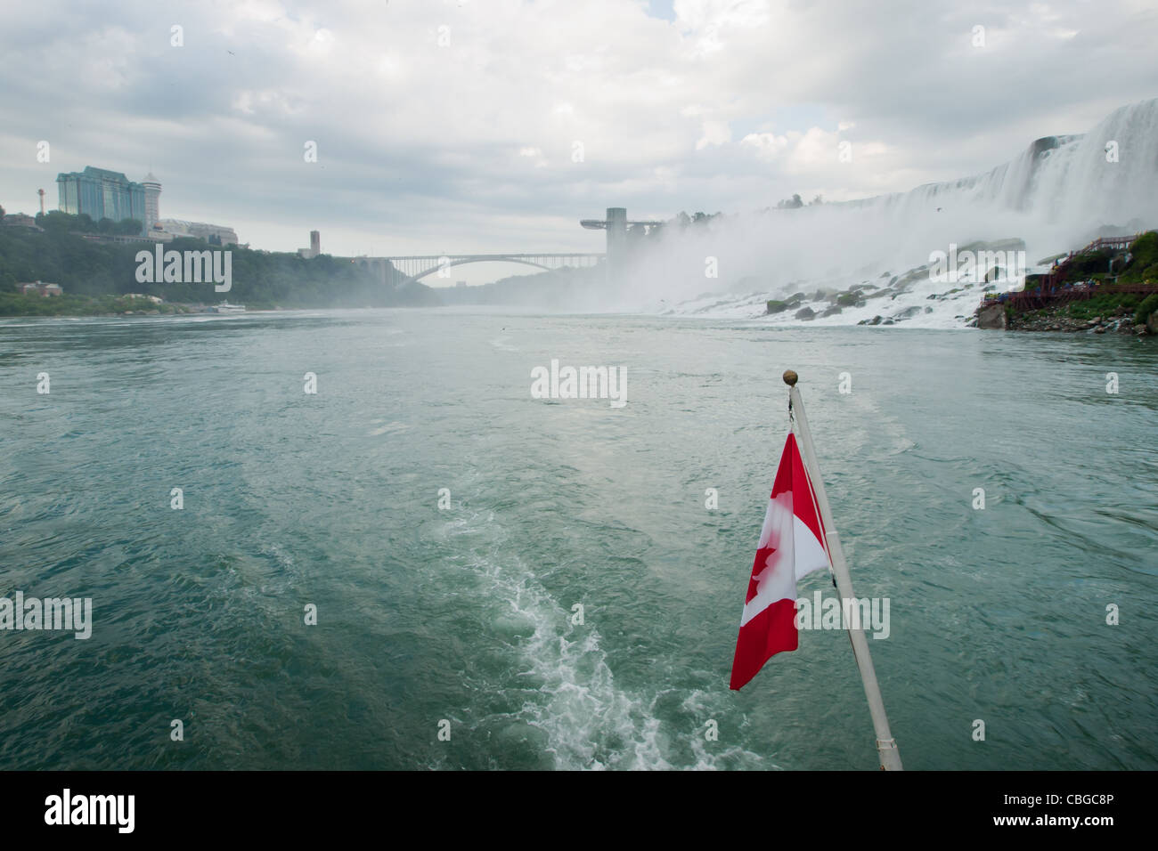 Die kanadische Flagge flattert von hinten von einem Ausflugsboot mit Niagara Falls im Hintergrund. Stockfoto