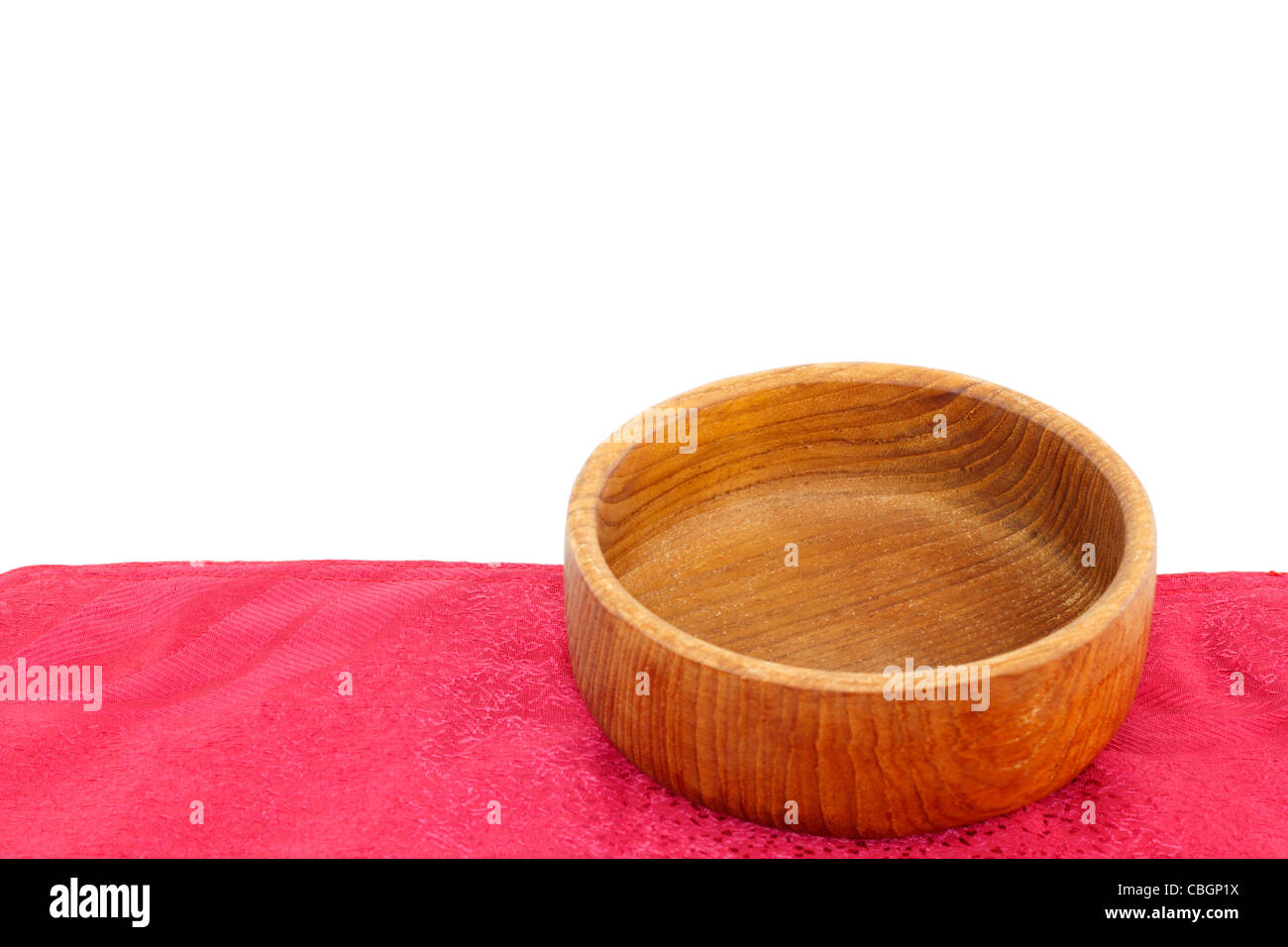 Leere Teak Holz Schüssel auf einer roten Platz-Matte isoliert auf einem weißen Hintergrund. Kleine Runde Holzschale close-up auf einem roten Tuch Tischset vor weiß. Stockfoto