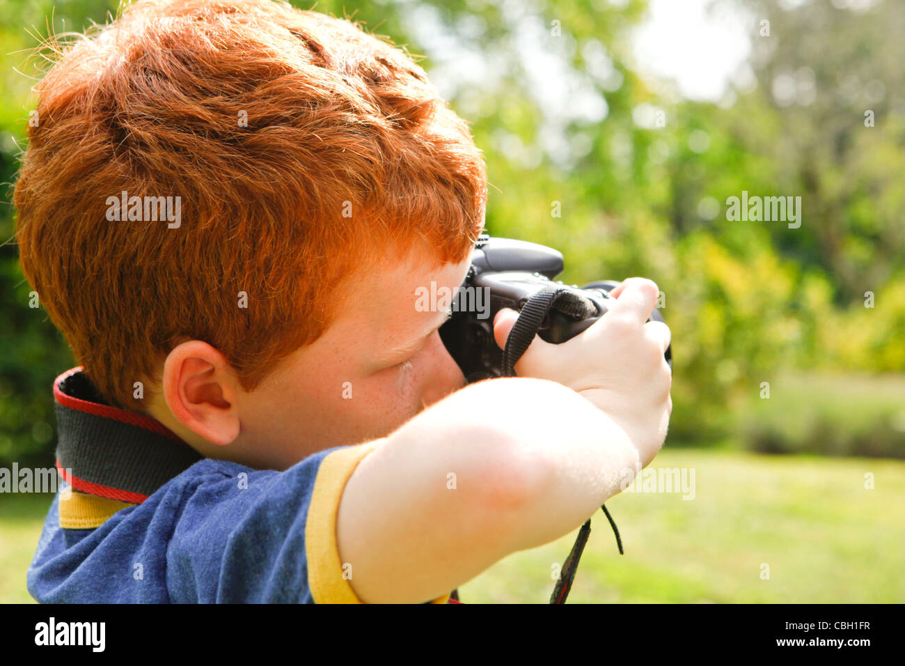 Ein kleiner Junge im Alter von 7, mit einer digitalen SLR-Kamera in einem sonnigen Garten. Stockfoto