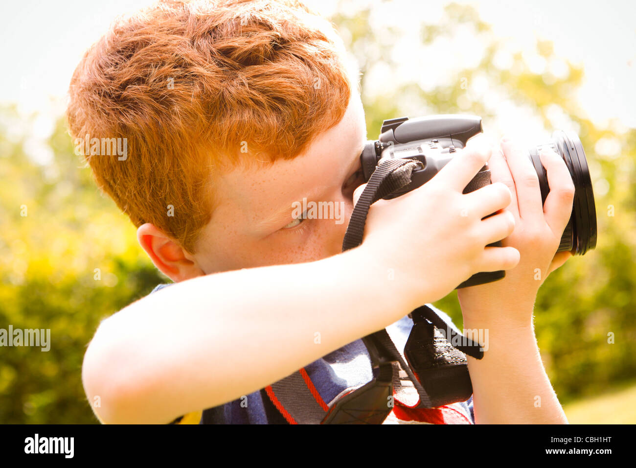 Ein kleiner Junge im Alter von 7, mit einer digitalen SLR-Kamera in einem sonnigen Garten. Stockfoto