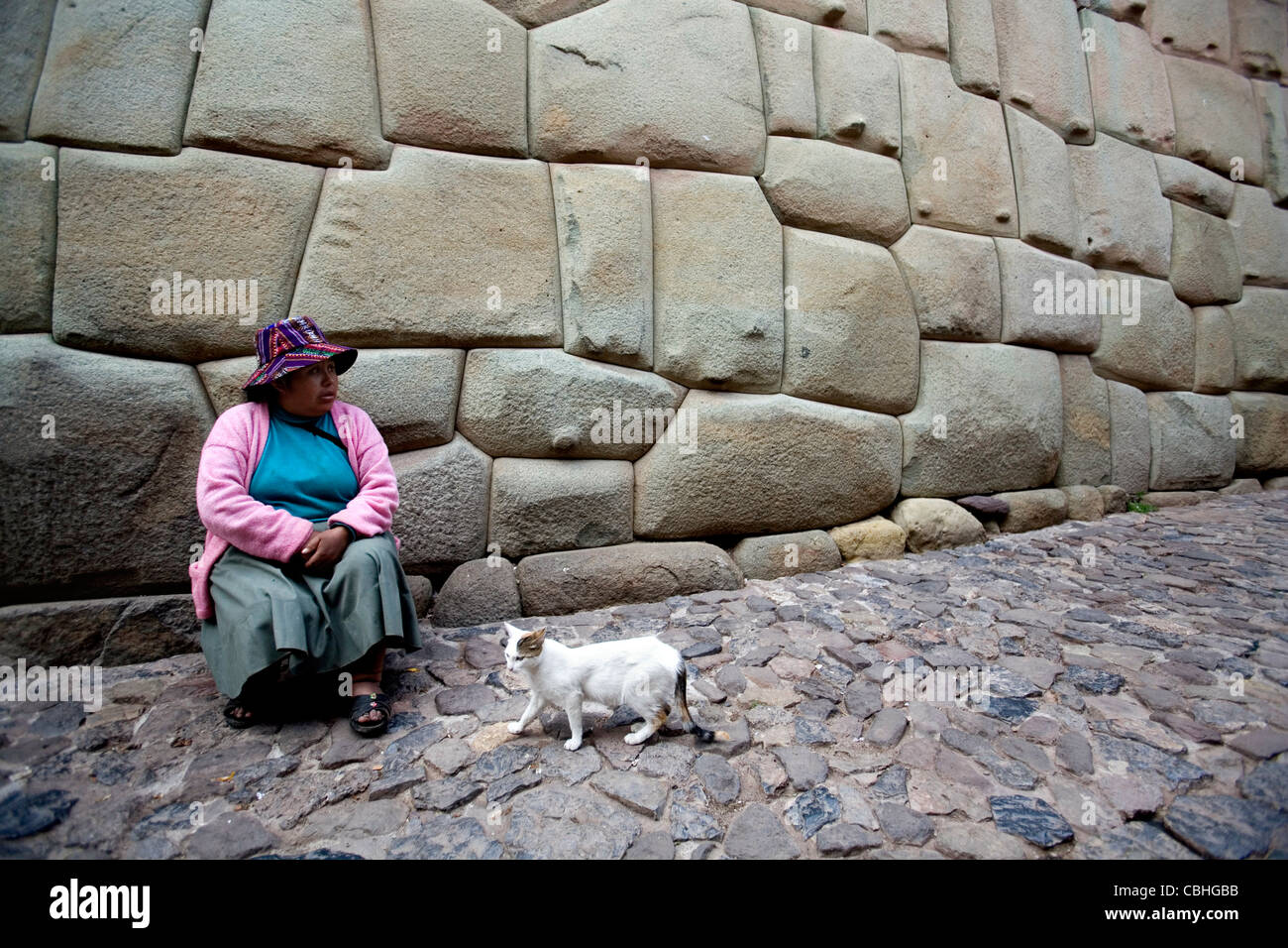 Indische Frau sitzt unter der Palast des Inca Roca-Seitenwand in Cusco, Peru Stockfoto