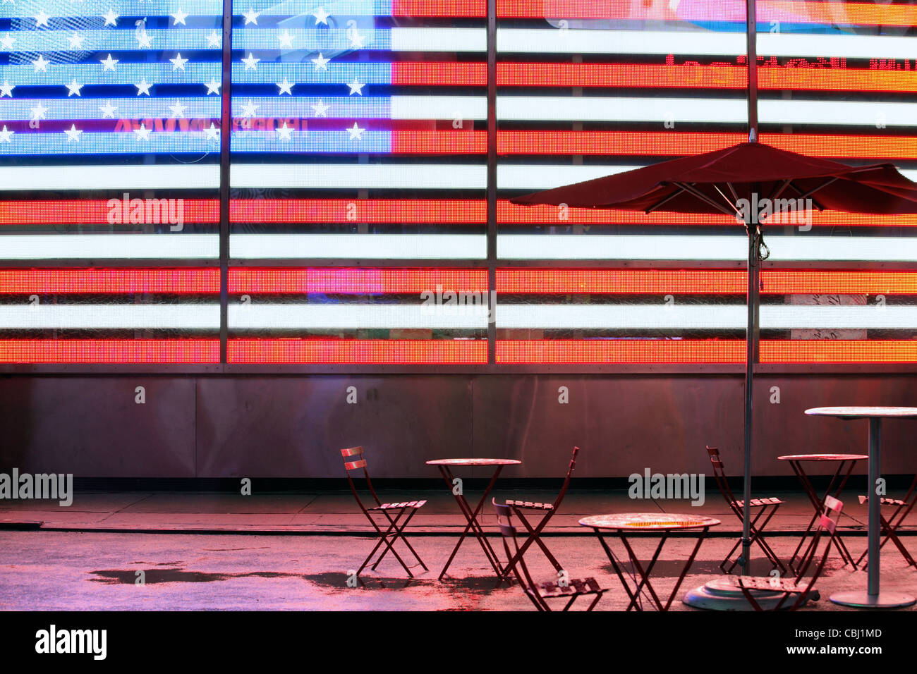 Leere Tische und Sonnenschirm vor beleuchtet Stars & Stripes, USA Flagge, Times Square, New York City, NY, USA Stockfoto