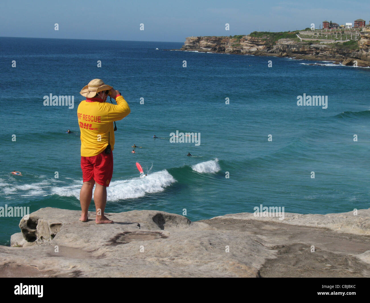 Mann beobachtet trägt Hut und Life Guard Kleidung Strand Bohrer von Klippe über dem Bondi Beach, Australien mit dem Fernglas zu retten Stockfoto