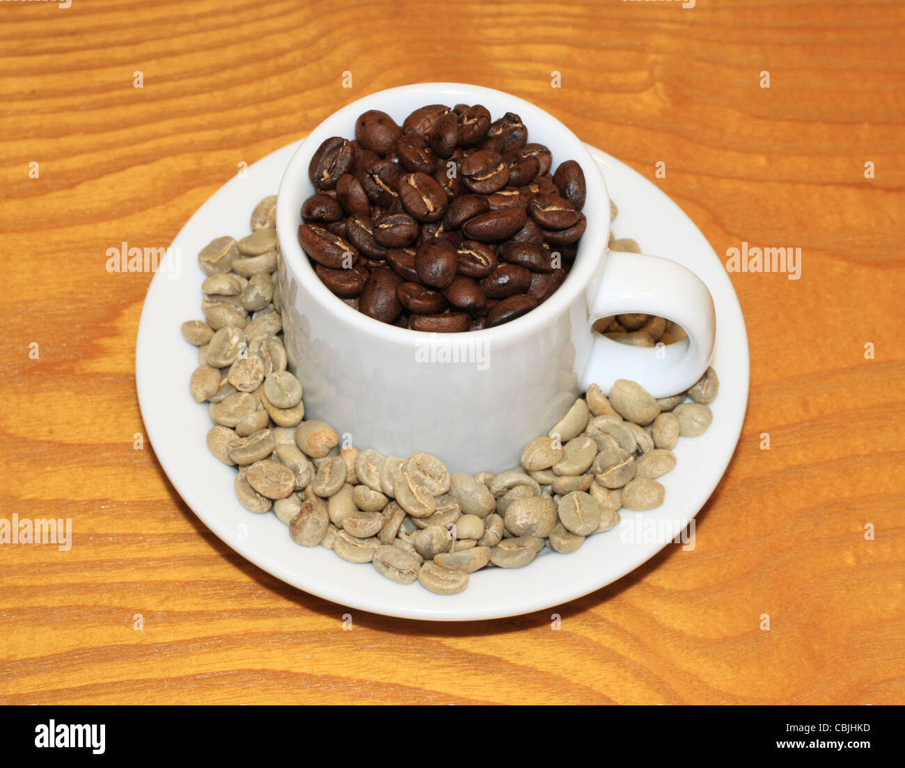 kleine Tasse geröstete Kaffeebohnen mit grünen Bohnen in die Untertasse auf Holz Hintergrund Stockfoto