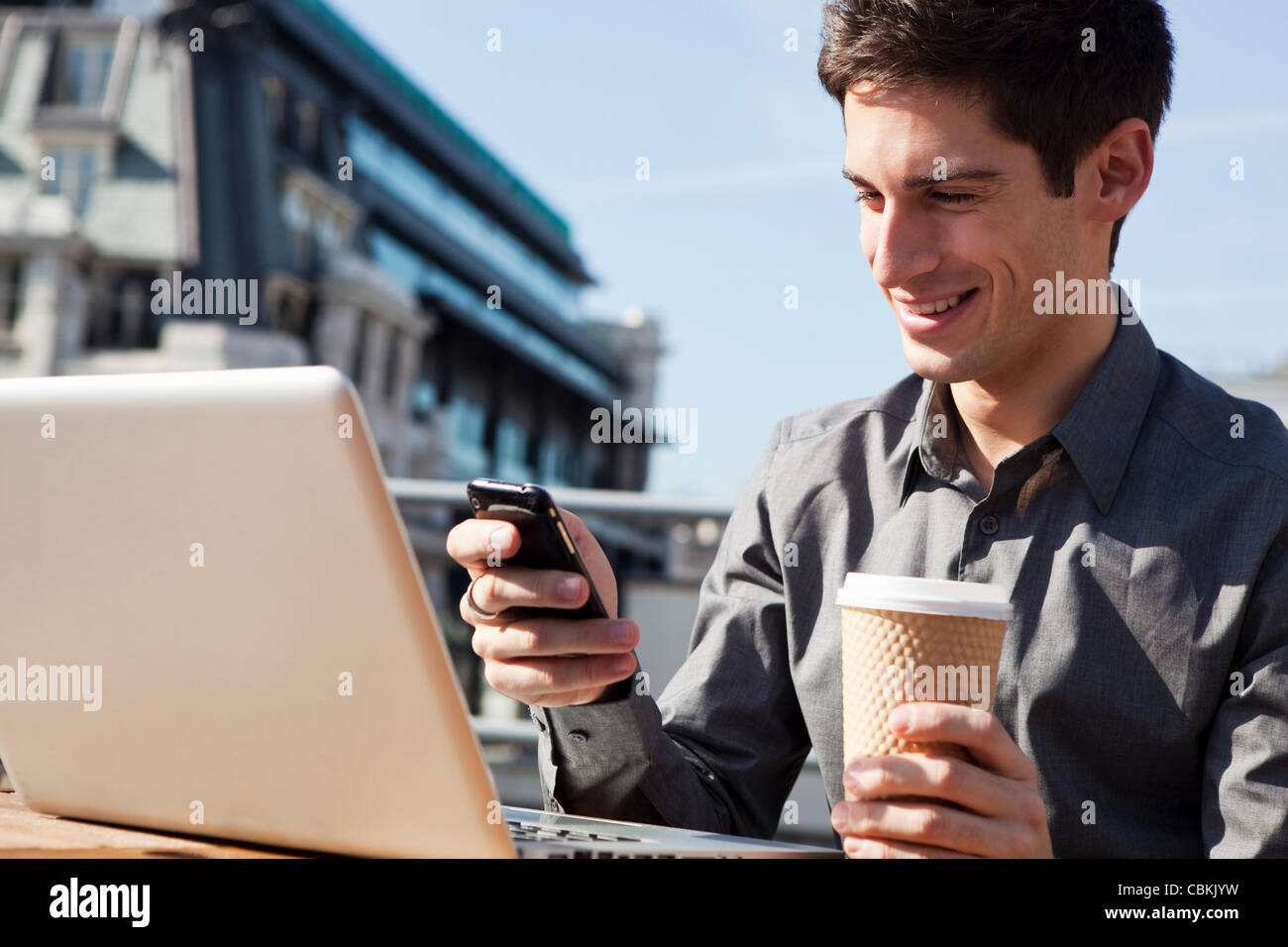 Junger Mann arbeiten im Freien mit seinem Laptop und Handy Stockfoto