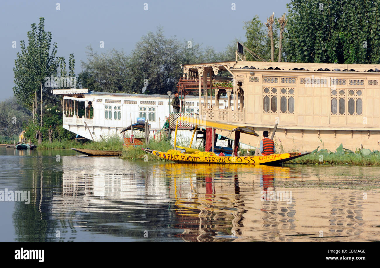 Eine gelbe Shikara, kleine Holzboot festgemacht durch ein Hausboot auf Dal-See. Die Shikara gehört zur Raat Fotodienste Stockfoto