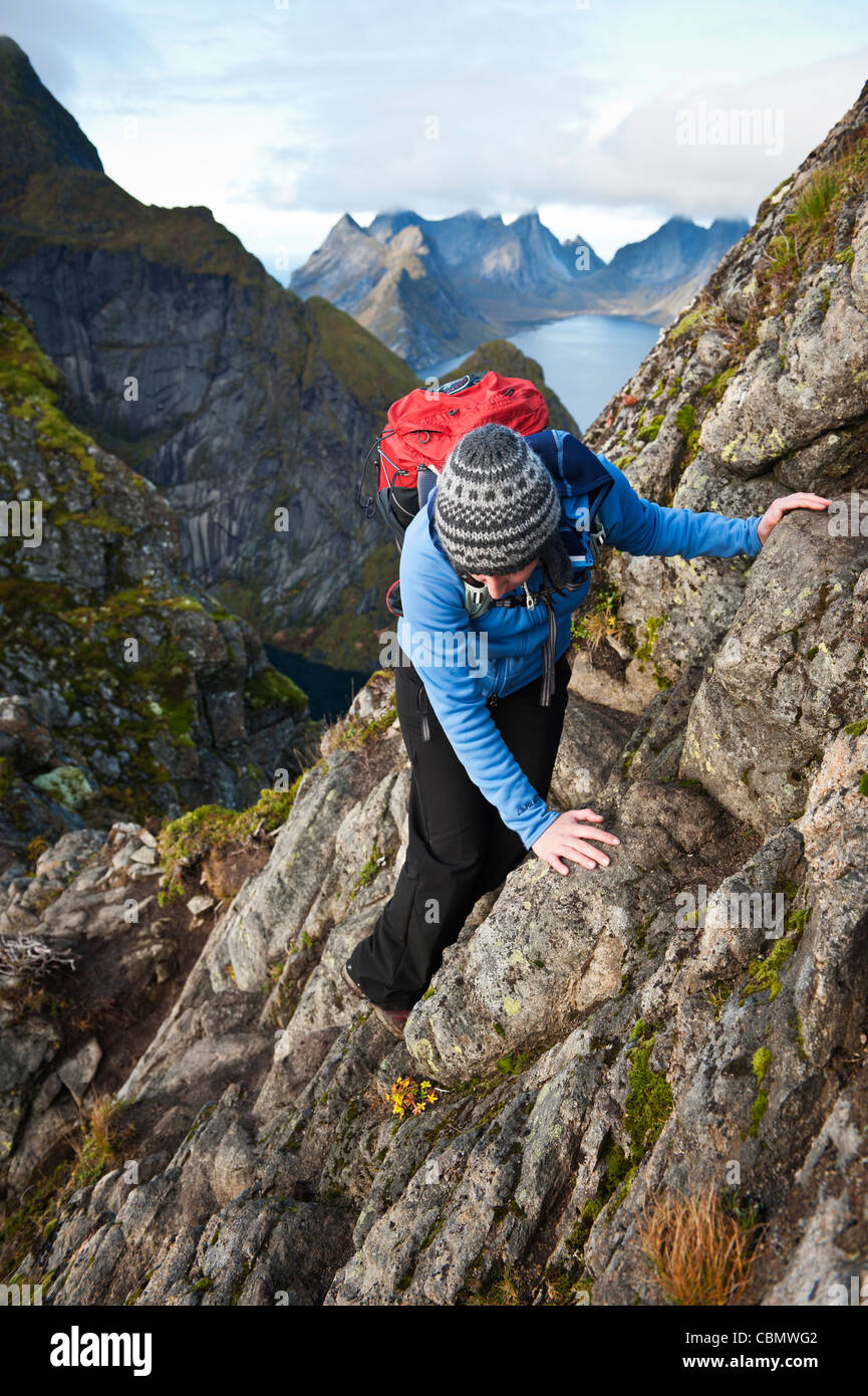 Weibliche Wanderer erklimmt Felsen nahe Gipfel des Reinebringen, Moskenesoy, Lofoten Inseln, Norwegen Stockfoto