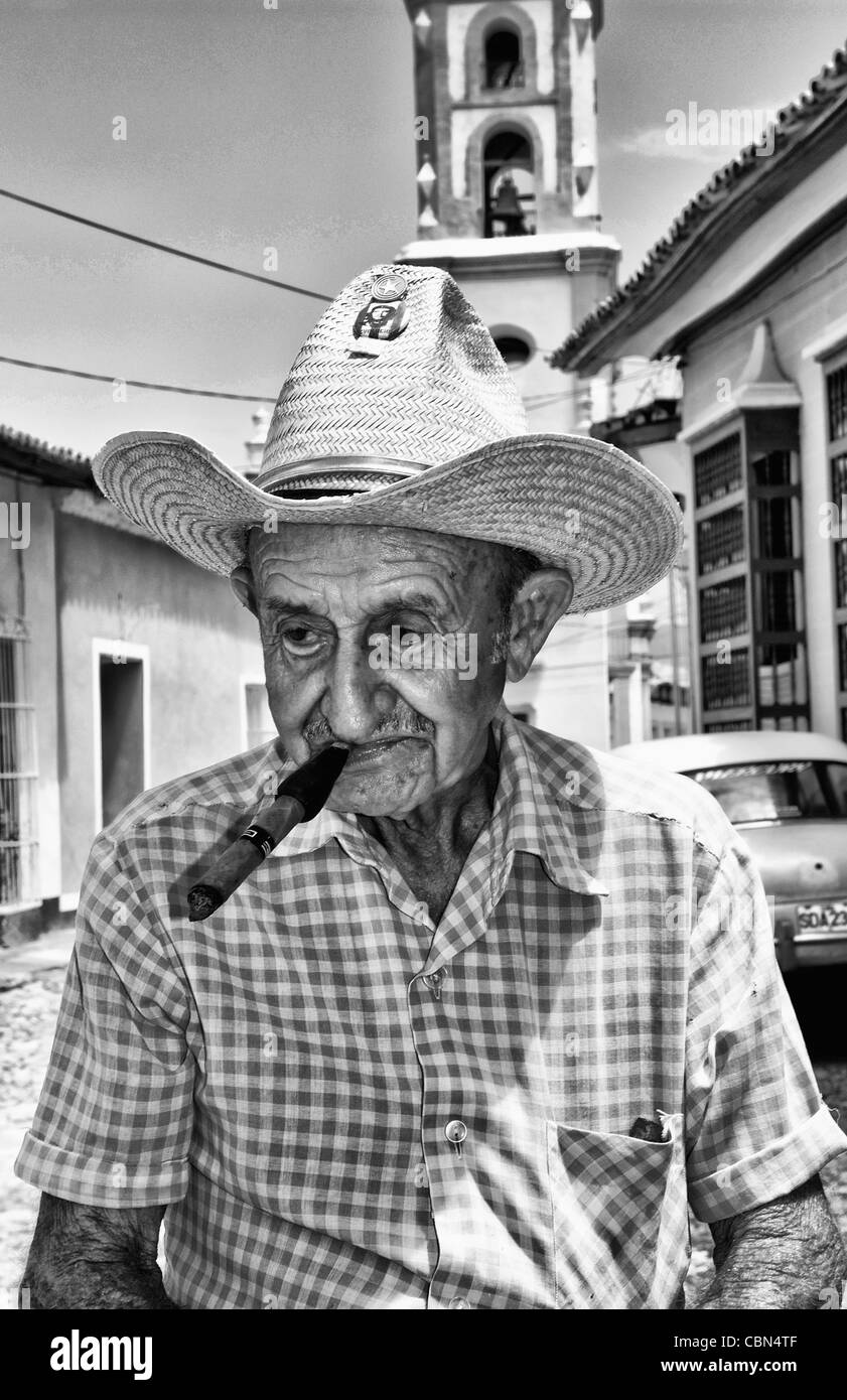 Alter Mann mit Zigarre auf Kopfsteinpflaster Szene mit alten Auto im Straßenbild mit alten Kirche der alten Kolonialstadt Trinidad Stockfoto