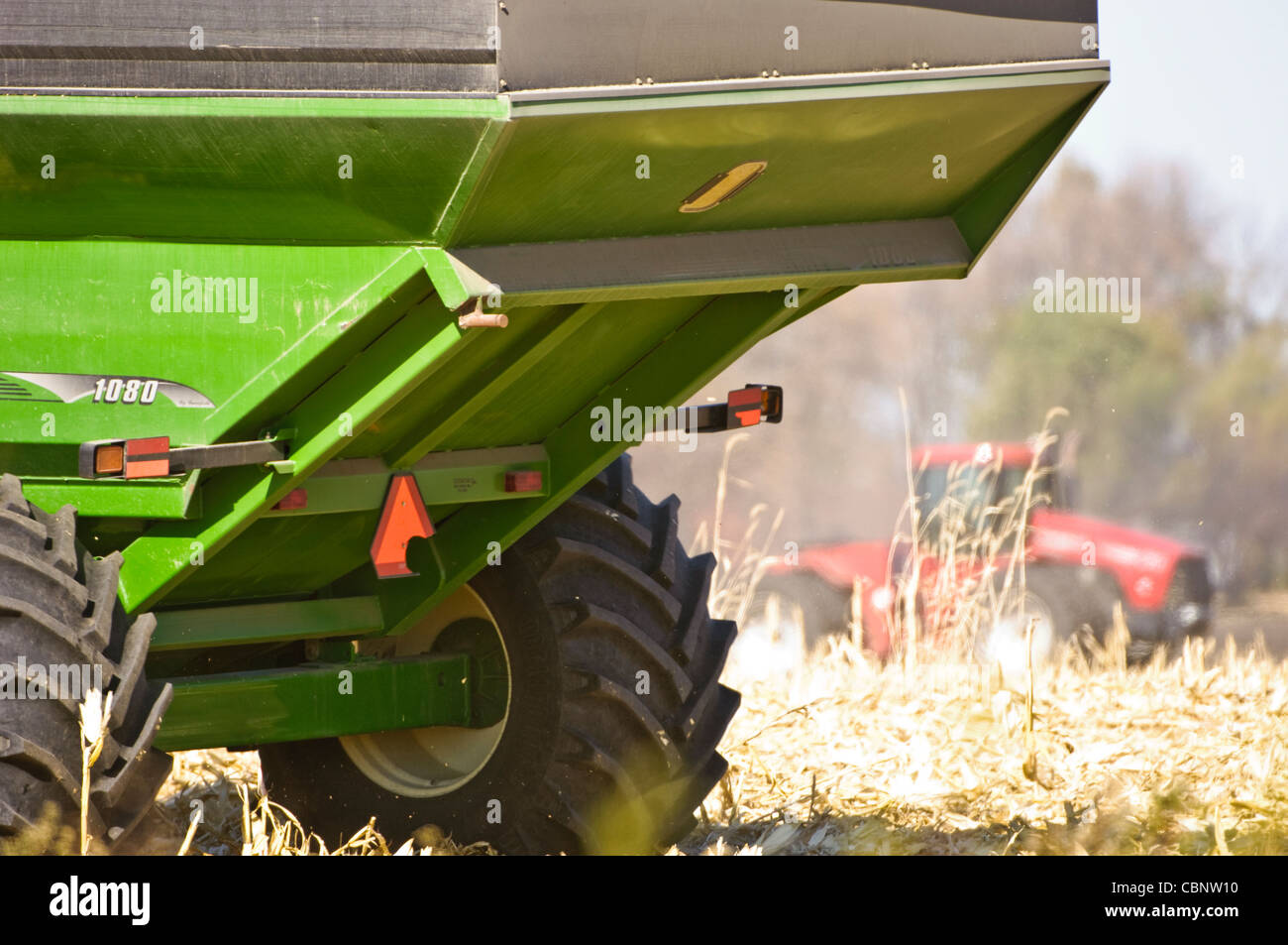 Ein schwere Wagen im Vordergrund erwartet Mais aus dem Mähdrescher während ein Traktors ein benachbartes Feld pflügt. Stockfoto