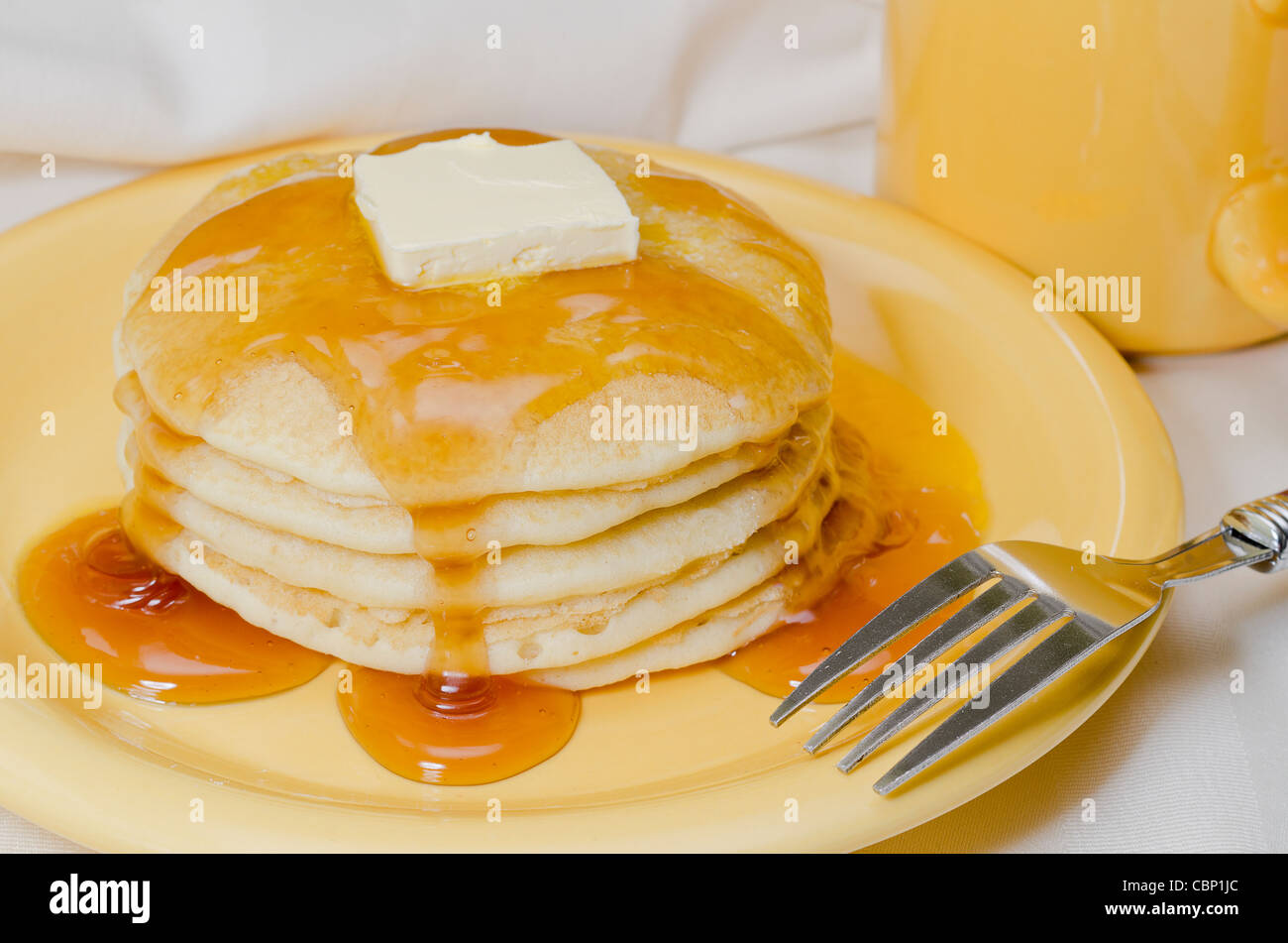 Stapel von Pfannkuchen mit Butter, Ahornsirup und Gabel. Kaffee im Hintergrund. Stockfoto