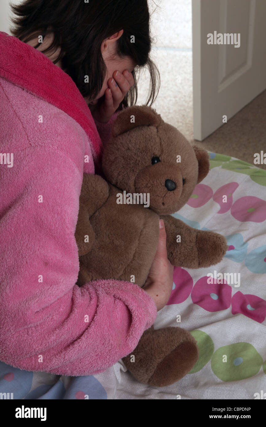 Über die Schulter Irl umklammert einen Teddybär sitzt auf ihrem Bett hand über die Augen Weinen. Stockfoto