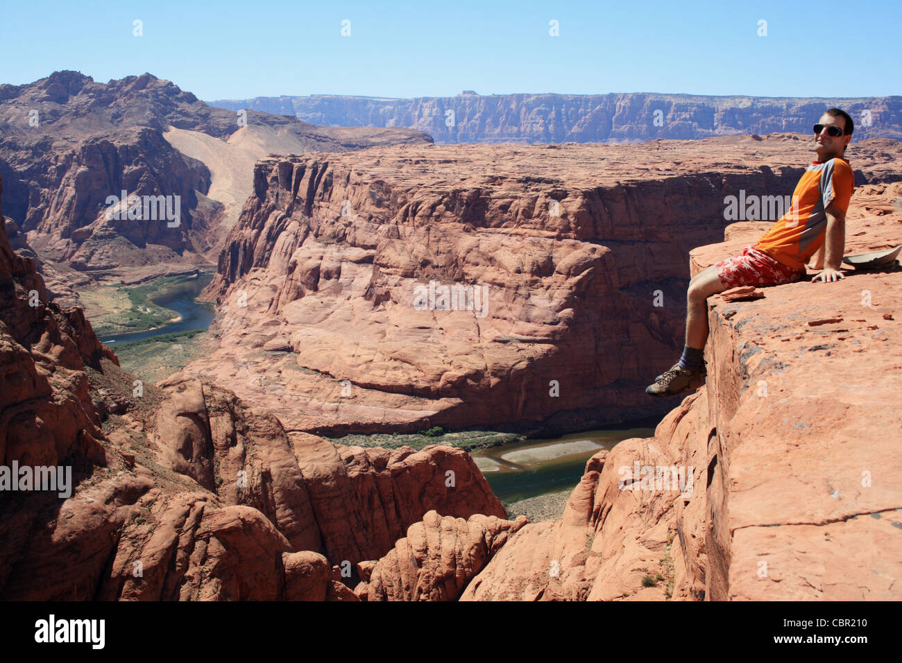 horizontale Bild von einem Mann sitzt auf dem Rand einer Sandstein-Klippe mit Blick auf Glen Canyon, Arizona Stockfoto