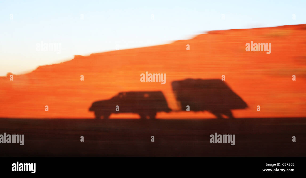 Schatten von einem rasenden LKW und Reisen Anhänger auf eine Bewegung verschwommene rote sandigen Damm Stockfoto