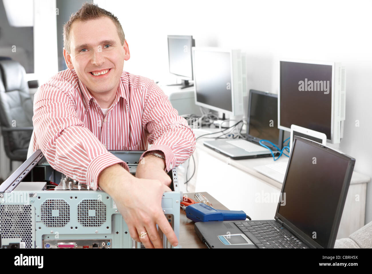 Mechaniker mit Computer. Monitore und andere Laptops im Hintergrund warten auf Service. Stockfoto