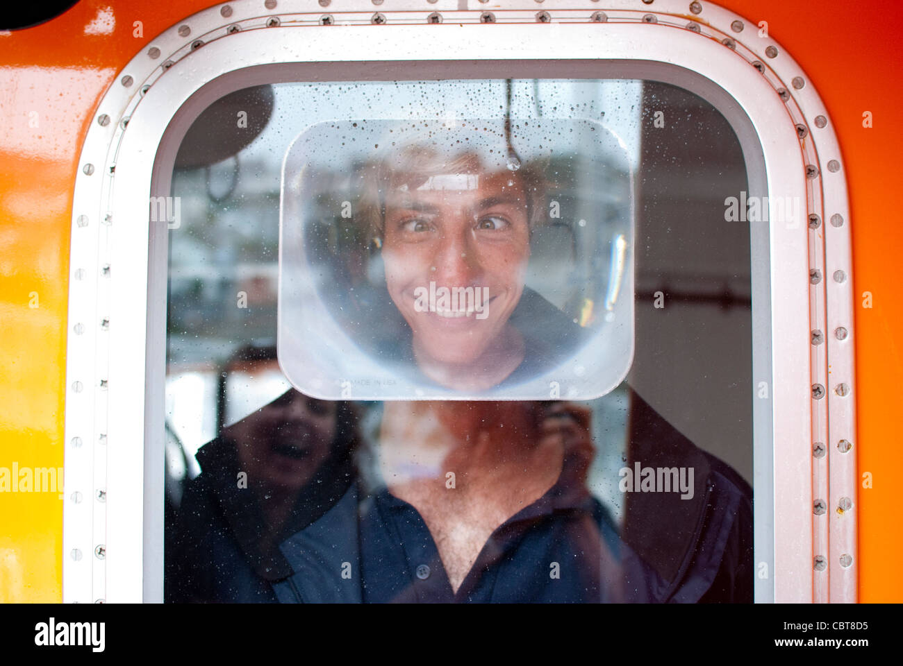 Ein RNLI-Member ziehen ein lustiges Gesicht aus dem Fenster ein Rettungsboot. Stockfoto
