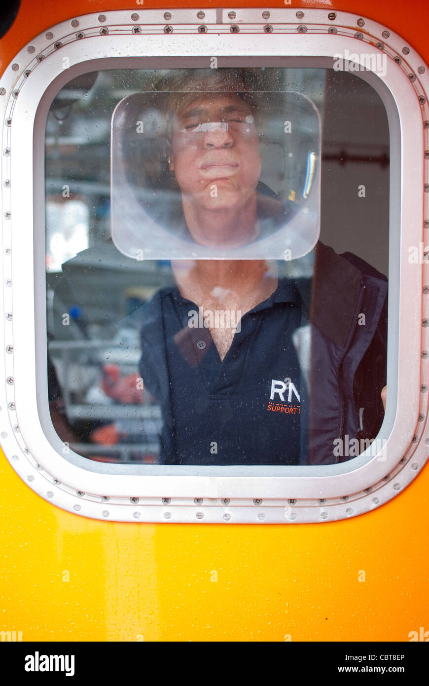 Ein RNLI-Member ziehen ein lustiges Gesicht aus dem Fenster ein Rettungsboot. Stockfoto