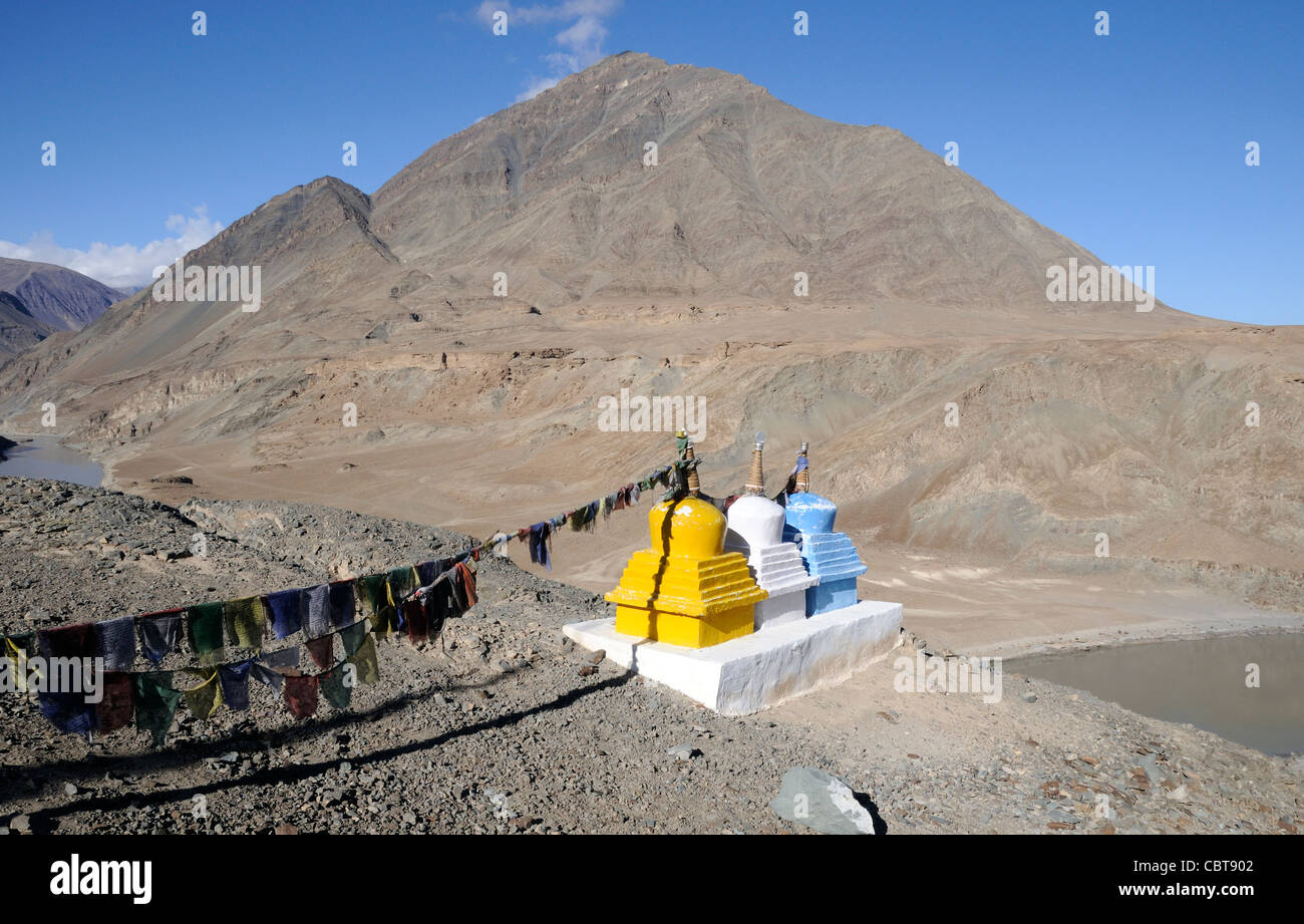 Gebetsfahnen und drei farbige Chörten oder Stupas markieren den Zusammenfluss des Flusses Zanskar und Indus in der Nähe von Nimu. Stockfoto