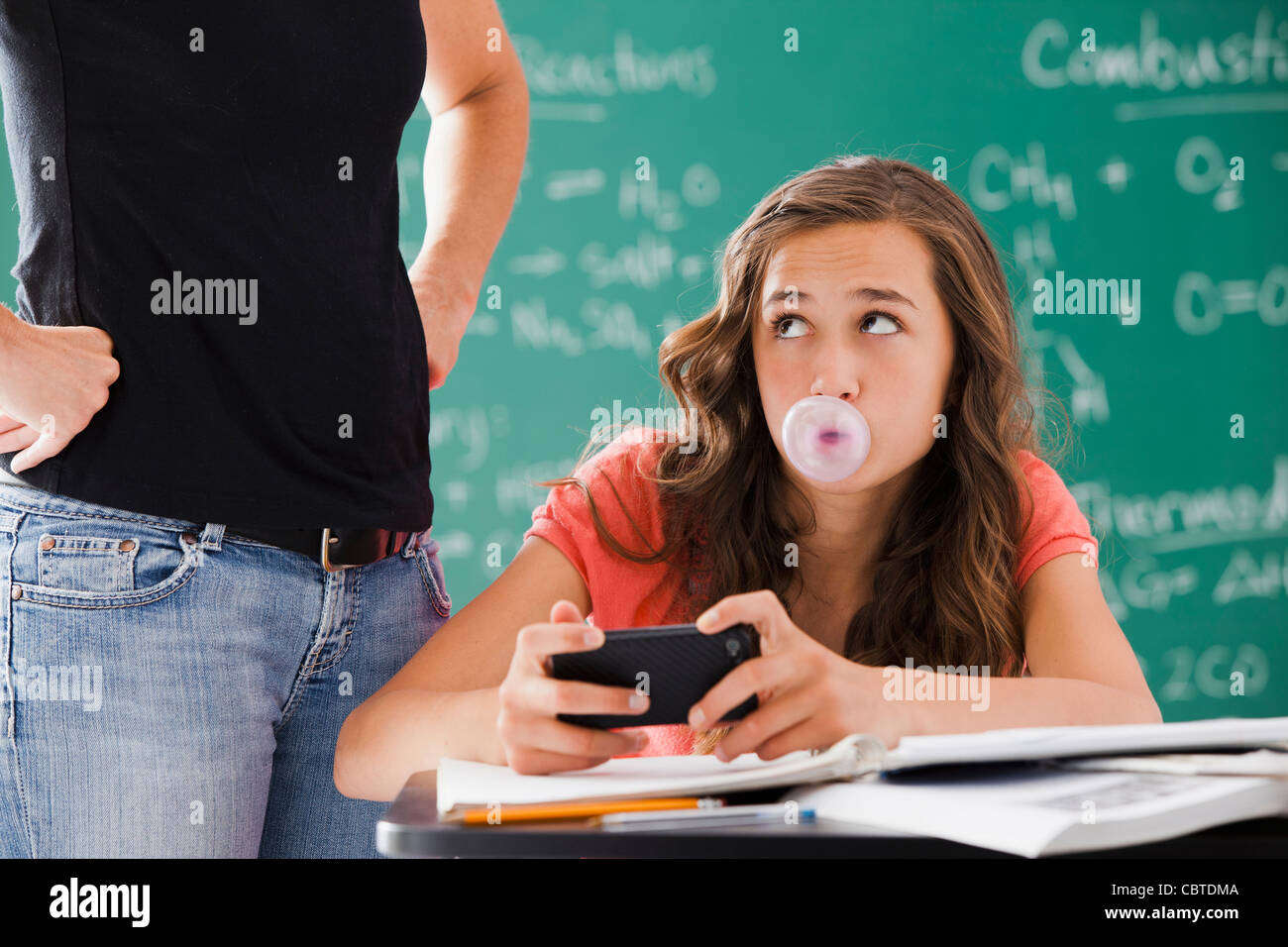 Frustrierte Lehrer beobachten Schüler mit Handy und Kaugummi Stockfoto