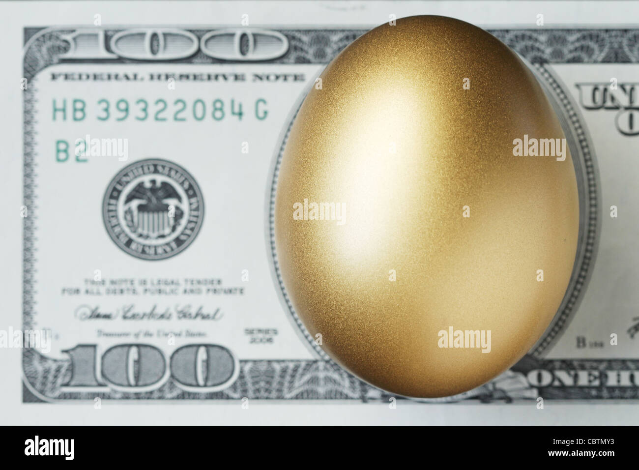 Ein goldenes Ei mit 100 Dollarnote im Hintergrund. (Geringe Schärfentiefe) Stockfoto
