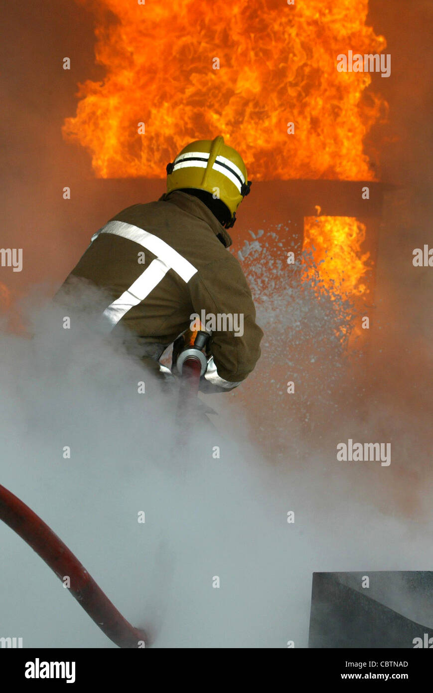 Ein einsamer Feuerwehrmann kämpft eine Flamme inmitten von Hitze und Rauch Stockfoto