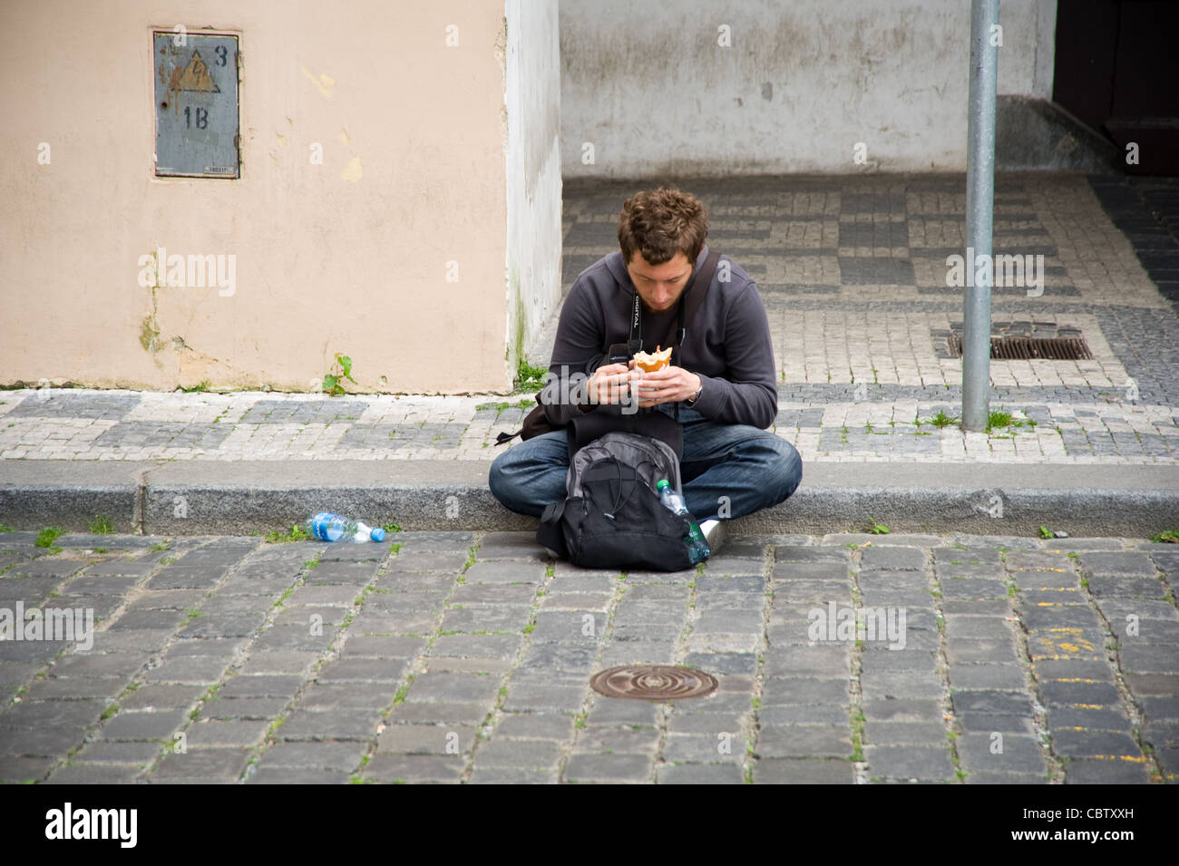 Junger Mann Touristen sitzen auf Bürgersteig Essen Sandwich Essen in Prag-Altstadt Stockfoto