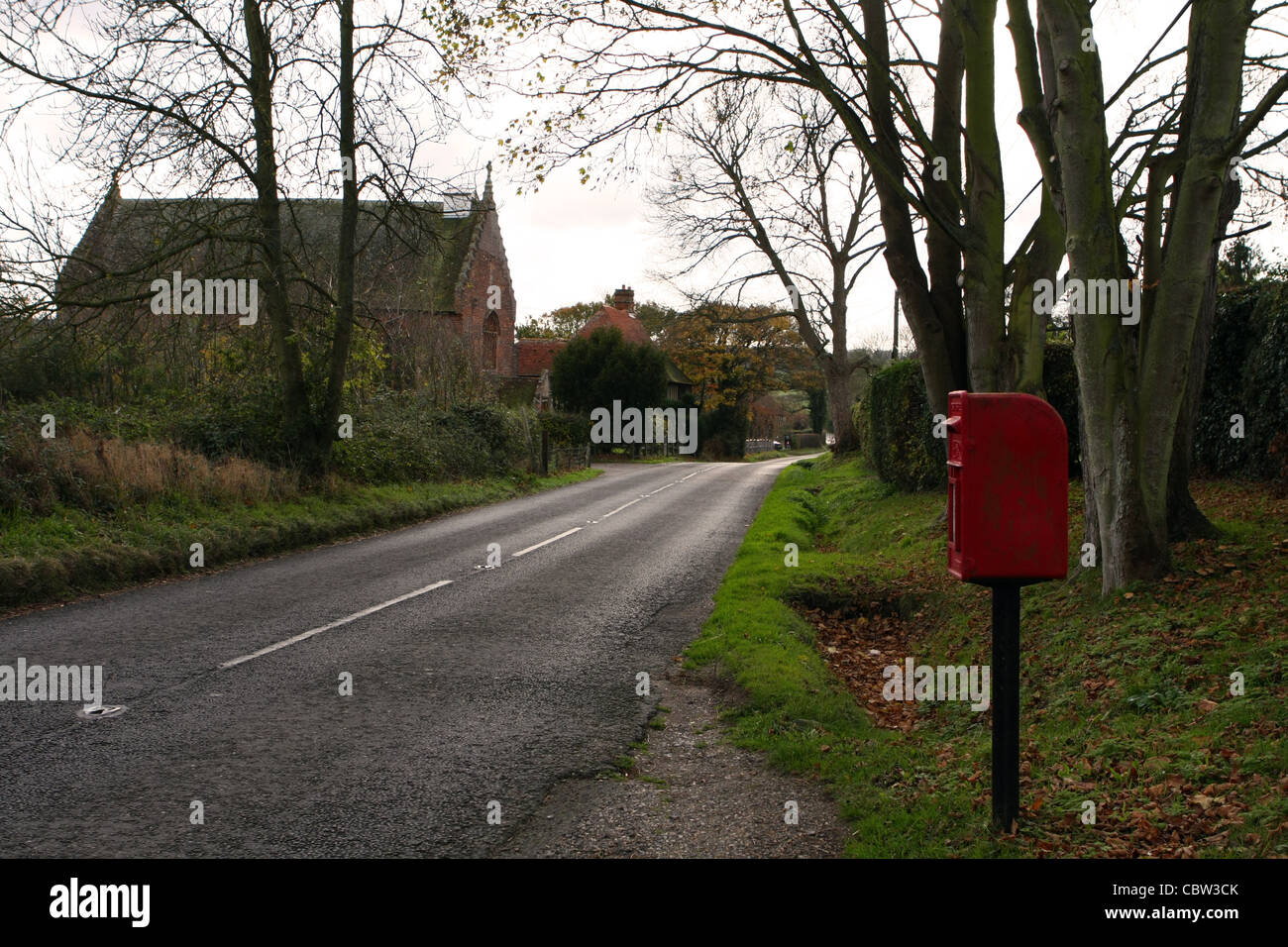 Blick entlang der Landstraße am kleinen Hythe in The Weald of Kent, England - ein Briefkasten auf der rechten Seite und einer kleinen Kirche auf der linken Seite Stockfoto