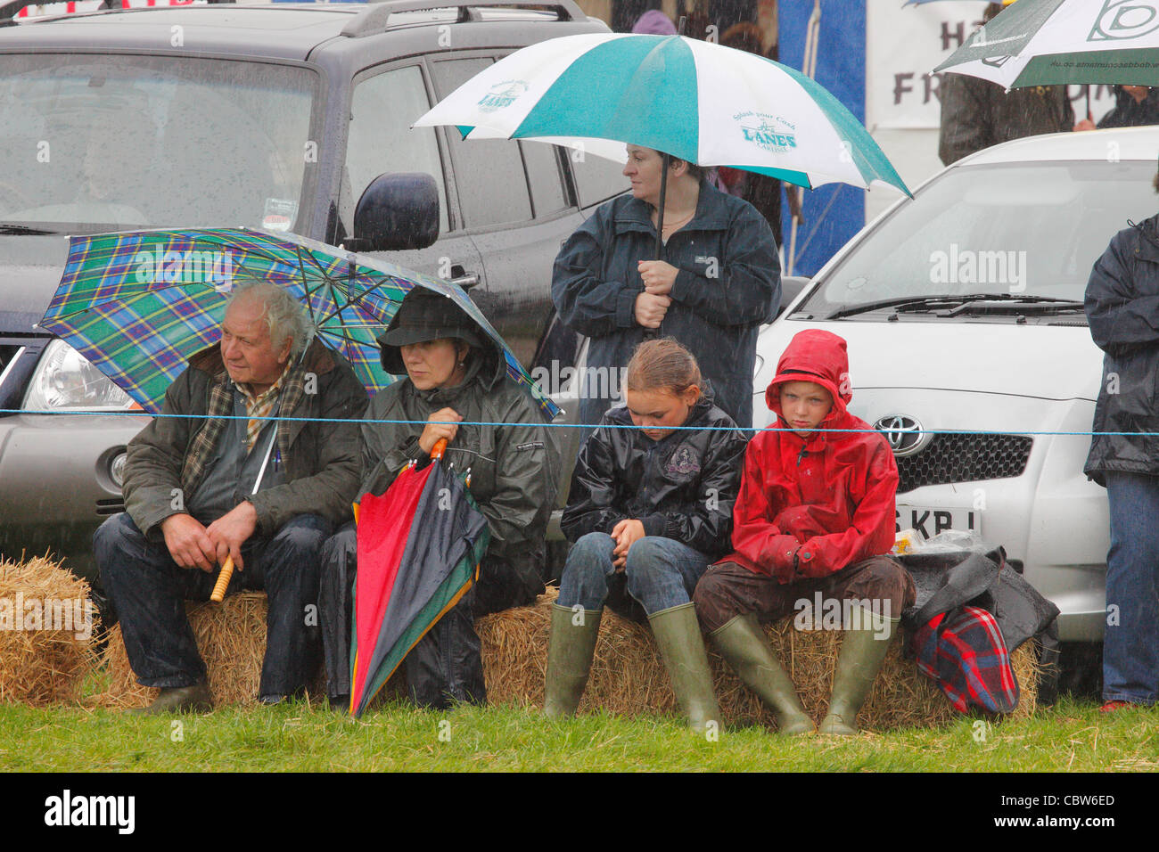 Zuschauer, die bergende unter Sonnenschirmen im Regen am Hesket Newmarket Agricultural Society Show, Calbeck, Cumbria, England, UK, Stockfoto