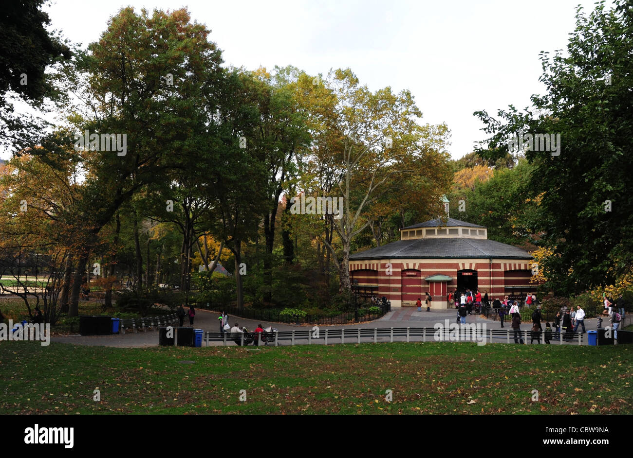 Herbstliche Parklandschaft Bäume anzeigen Personen stehend Plaza rote Ziegel Karussell Gebäude aus Mittenantrieb, Central Park South New York Stockfoto