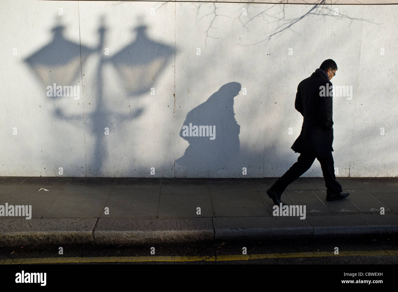 Mann zu Fuß auf dem Bürgersteig Schatten von altmodisch Lampe Pfosten vorbei Stockfoto