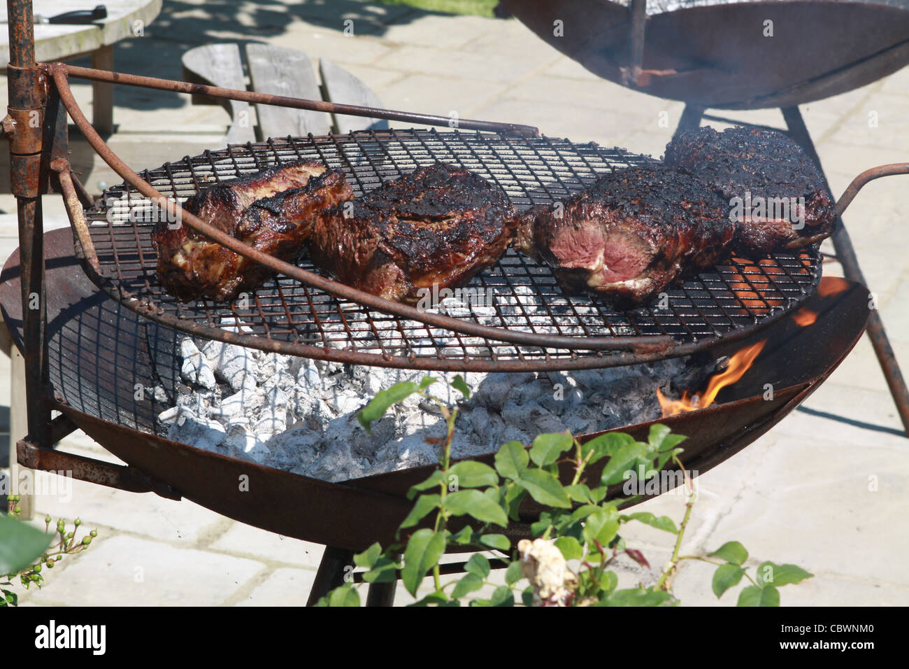 Rindfleisch Kochen auf großer Grill mit Flammen sichtbar vor dem dunklen Hintergrund Stockfoto