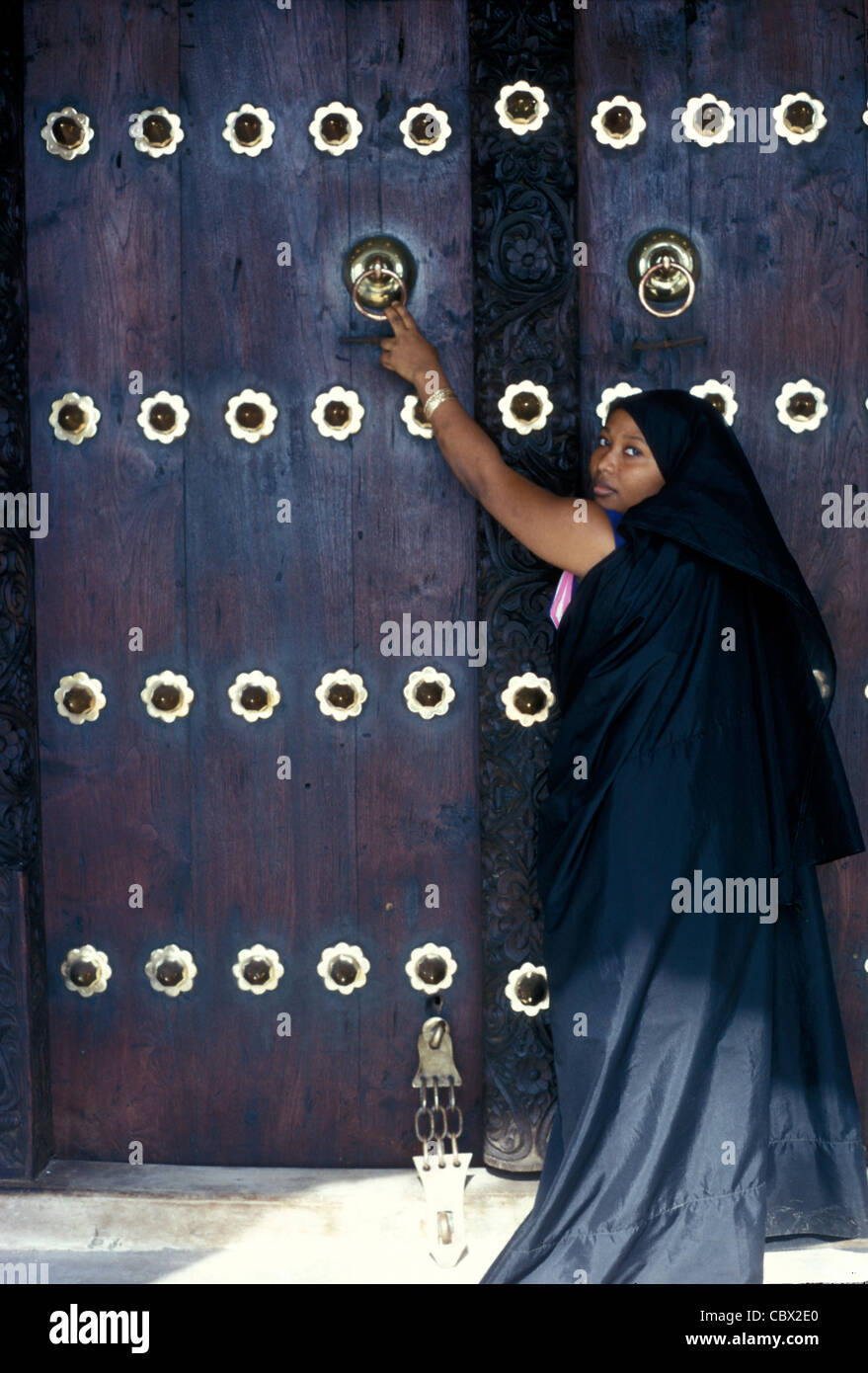 Große geschnitzte Tür aus Holz und Messing in Lamu Stadt mit Frauen in traditioneller arabischer Kleidung, Kenia Stockfoto